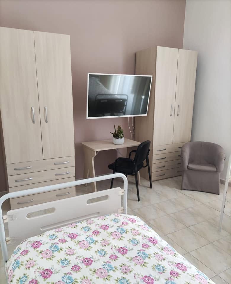 Camera d'ospedale con letto, scrivania, TV a parete, due armadi e una sedia.