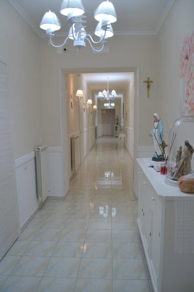 Luminoso corridoio con pavimento piastrellato lucido, pareti bianche, luci a soffitto e un piccolo altare o un'esposizione religiosa.