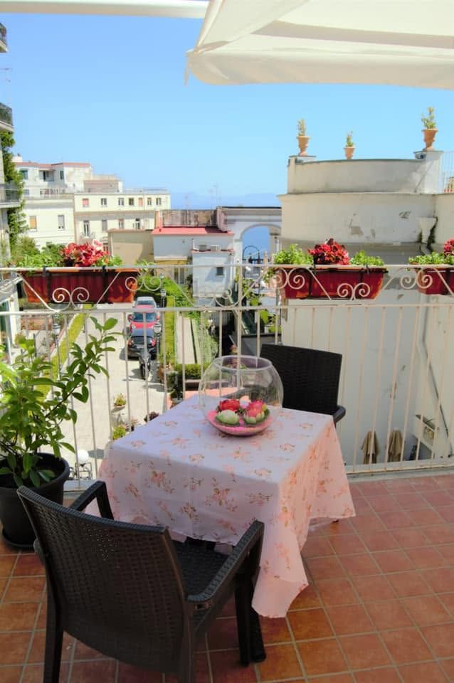 Tavolino da caffè sulla terrazza con cesto di frutta e sedie, con vista soleggiata sul mare.