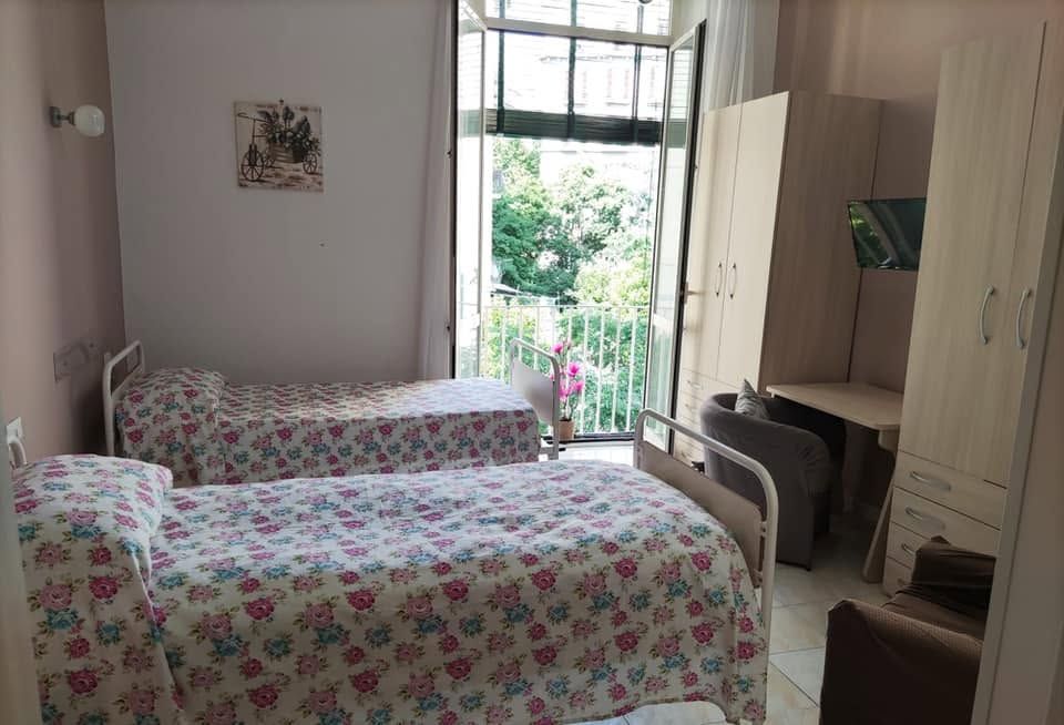 Piccola camera da letto con due letti a fiori, finestra aperta e armadio accanto a una scrivania.