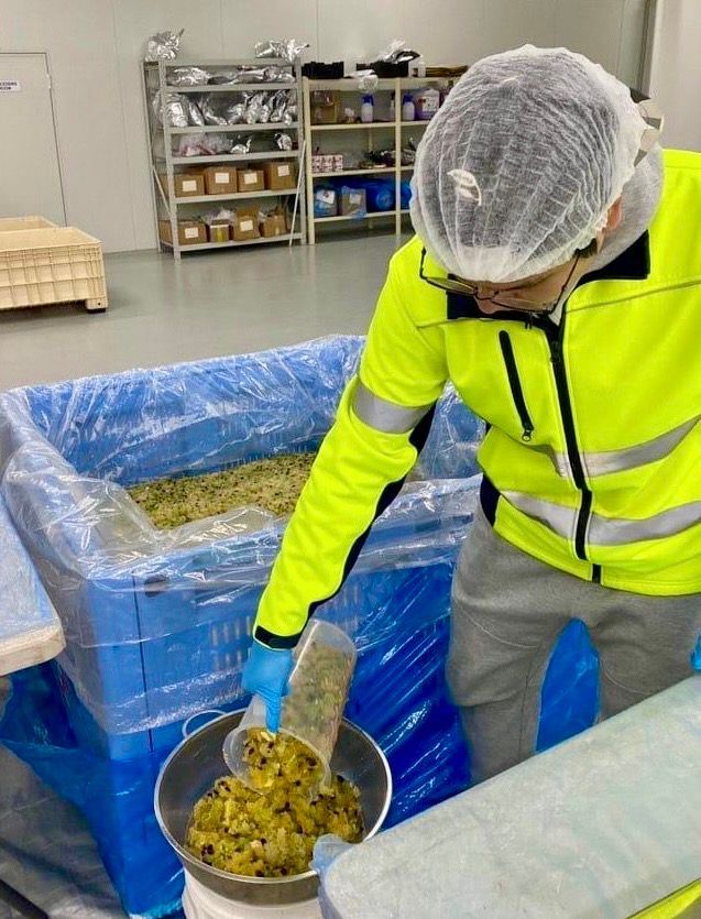 A man in a yellow jacket is pouring something into a bowl.