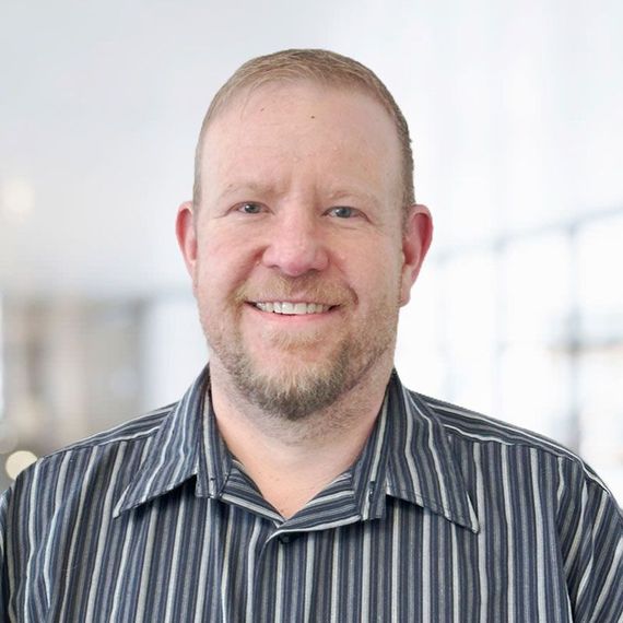 Smiling man in a striped shirt against a bright indoor background
