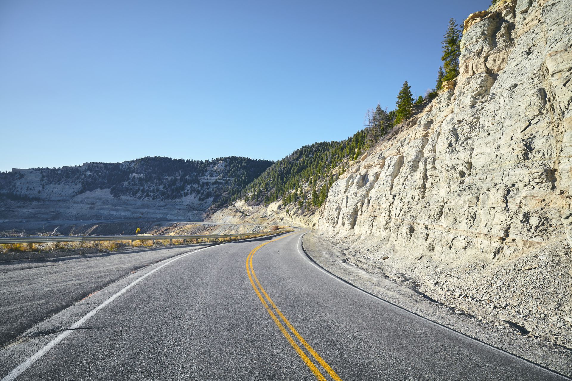 Winding mountain road beside a rocky cliff under a clear blue sky