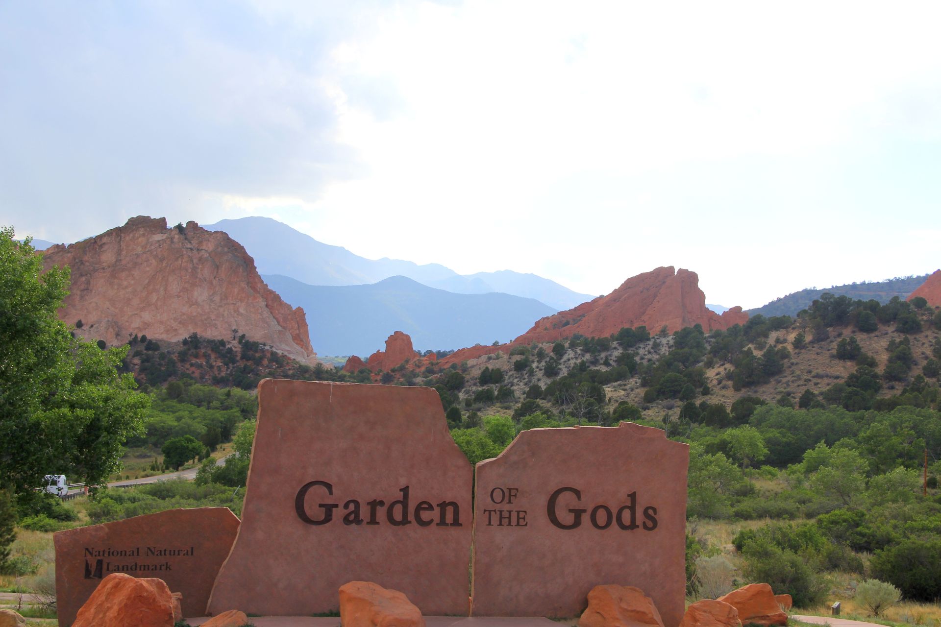 Garden of the Gods sign with red rock formations and green shrubs under a bright sky