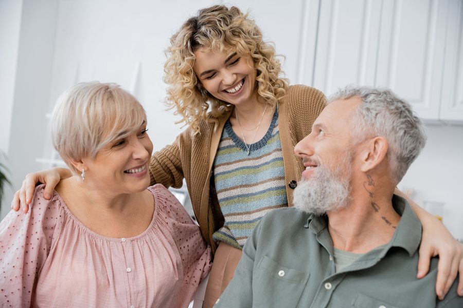 Three smiling people sitting together on a couch, with one standing behind them.