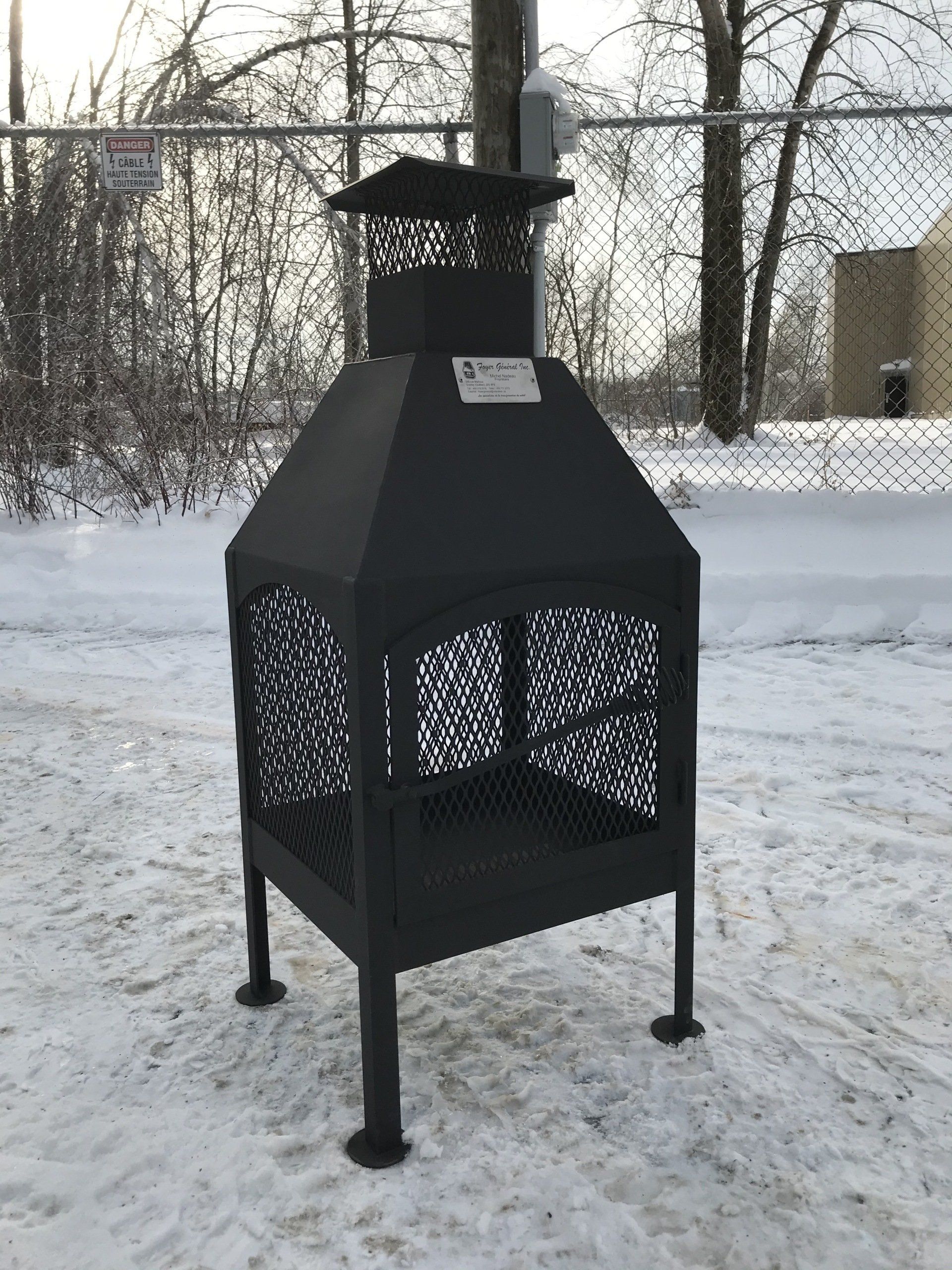 Foyer extérieur en métal noir sur un sol enneigé avec une clôture grillagée en arrière-plan.