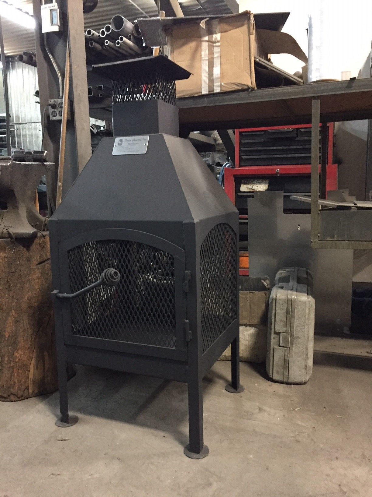 Foyer extérieur en métal noir avec porte grillagée, dans un atelier.