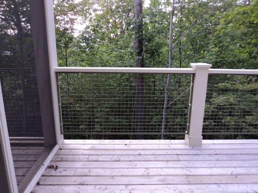 Terrasse avec garde-corps blanc et barrière grillagée, donnant sur les arbres.