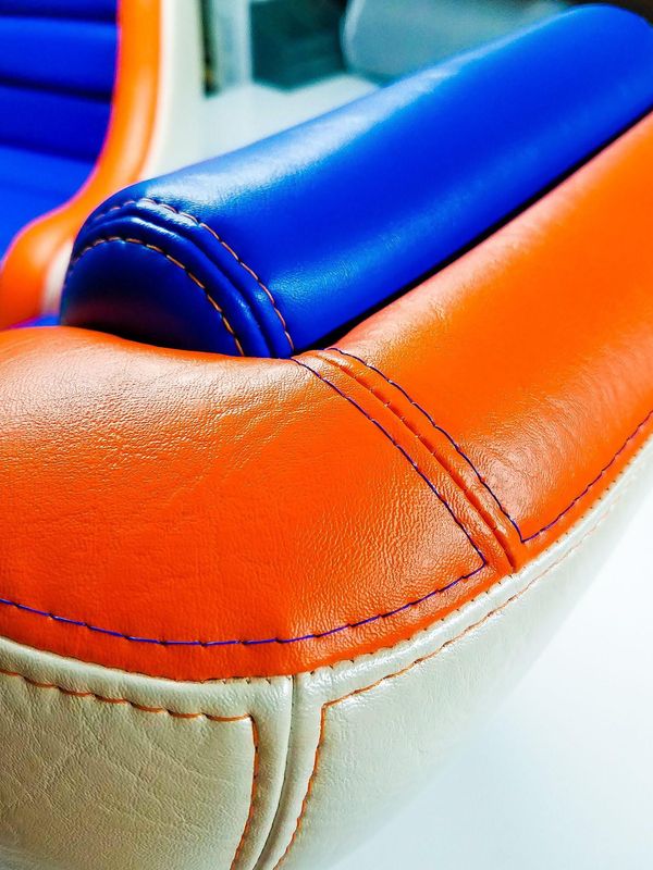 Close-up of colorful padded leather upholstery in blue, orange, and cream with stitched seams.