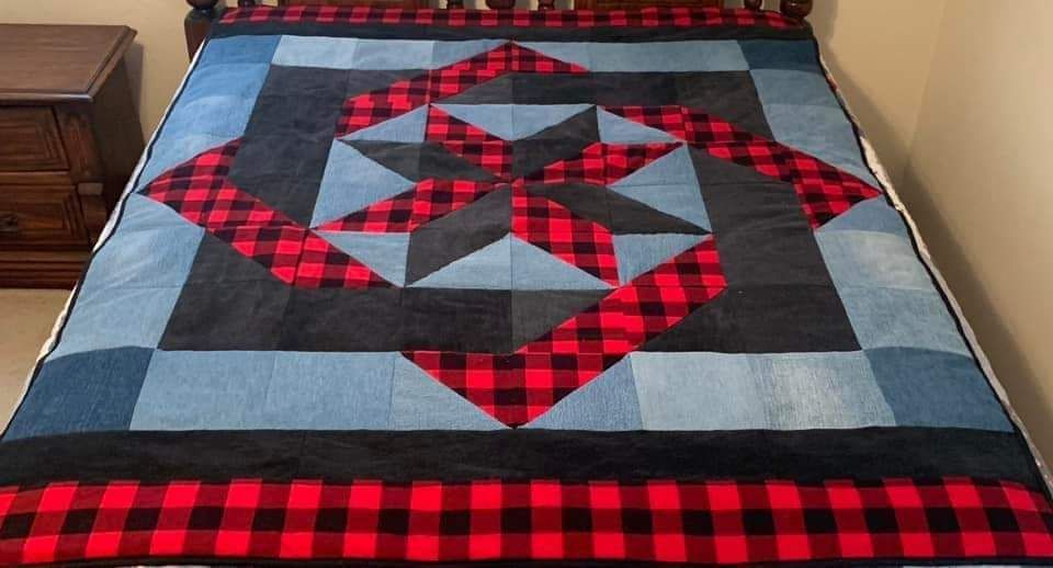 Neatly made bed with a gray, black, and red plaid patchwork quilt and matching border.