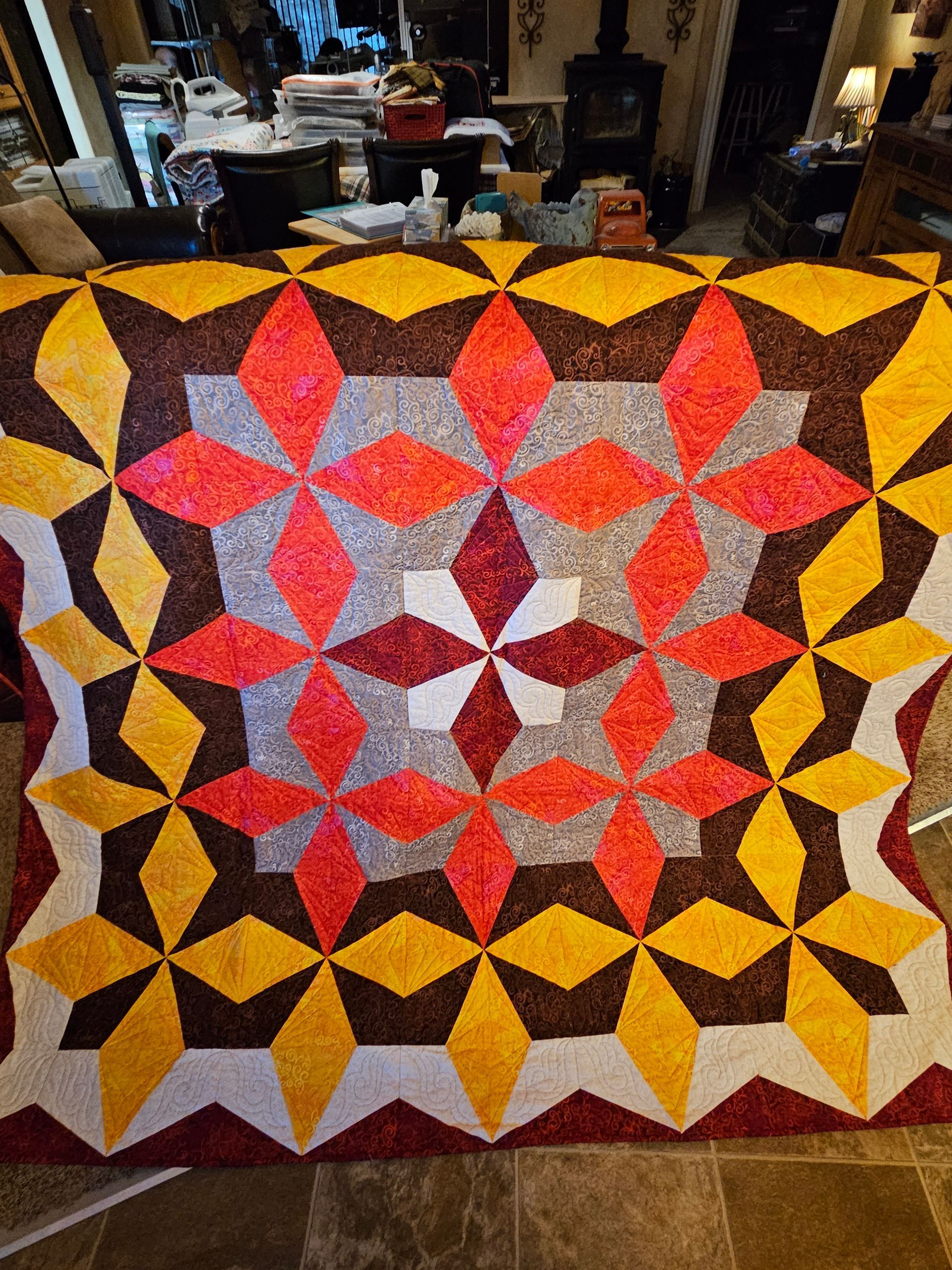 Colorful starburst patchwork quilt with red, pink, yellow, and white geometric patterns laid out indoors