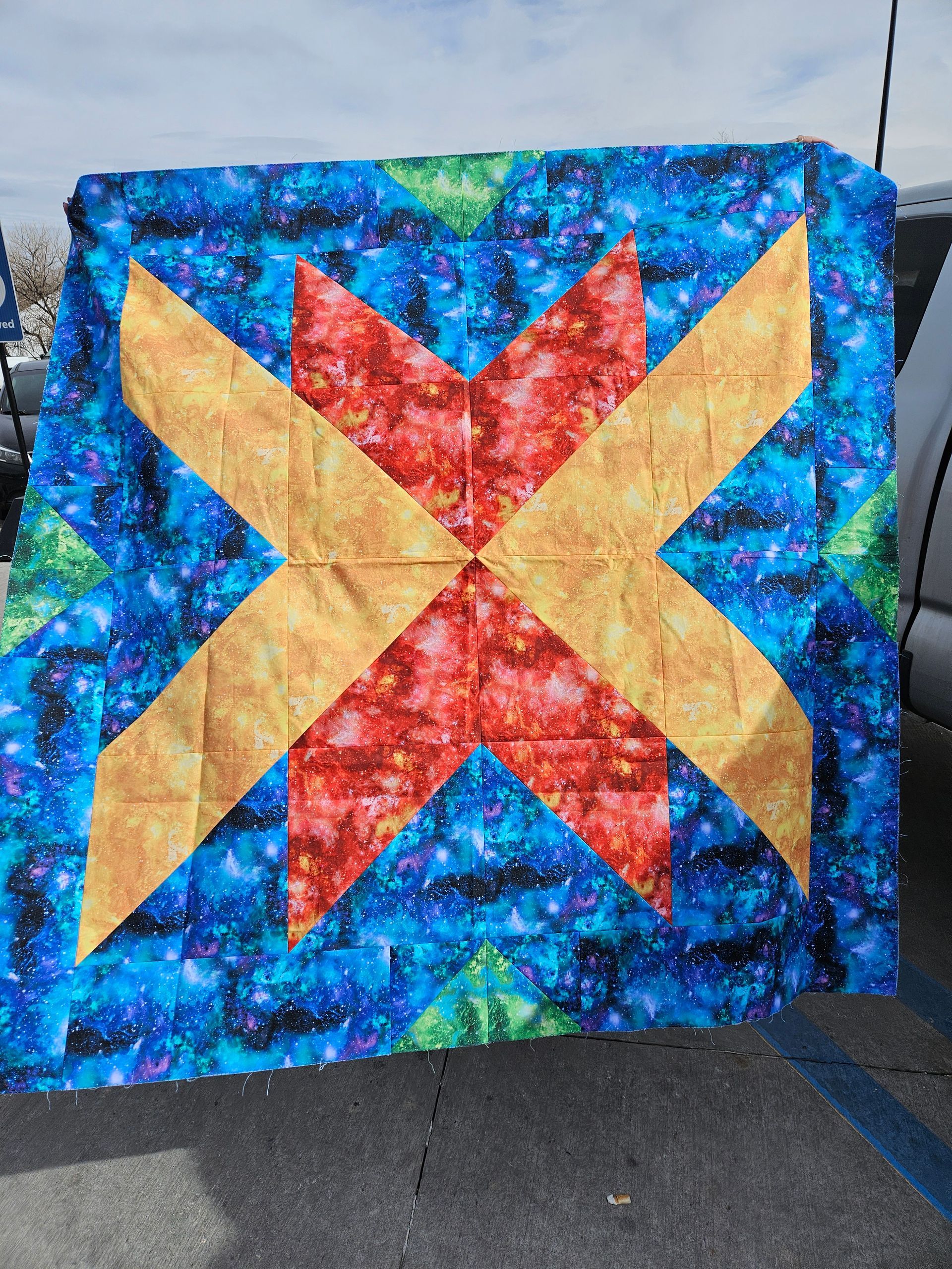 Blue quilt with a red and tan star pattern displayed outdoors on a fence