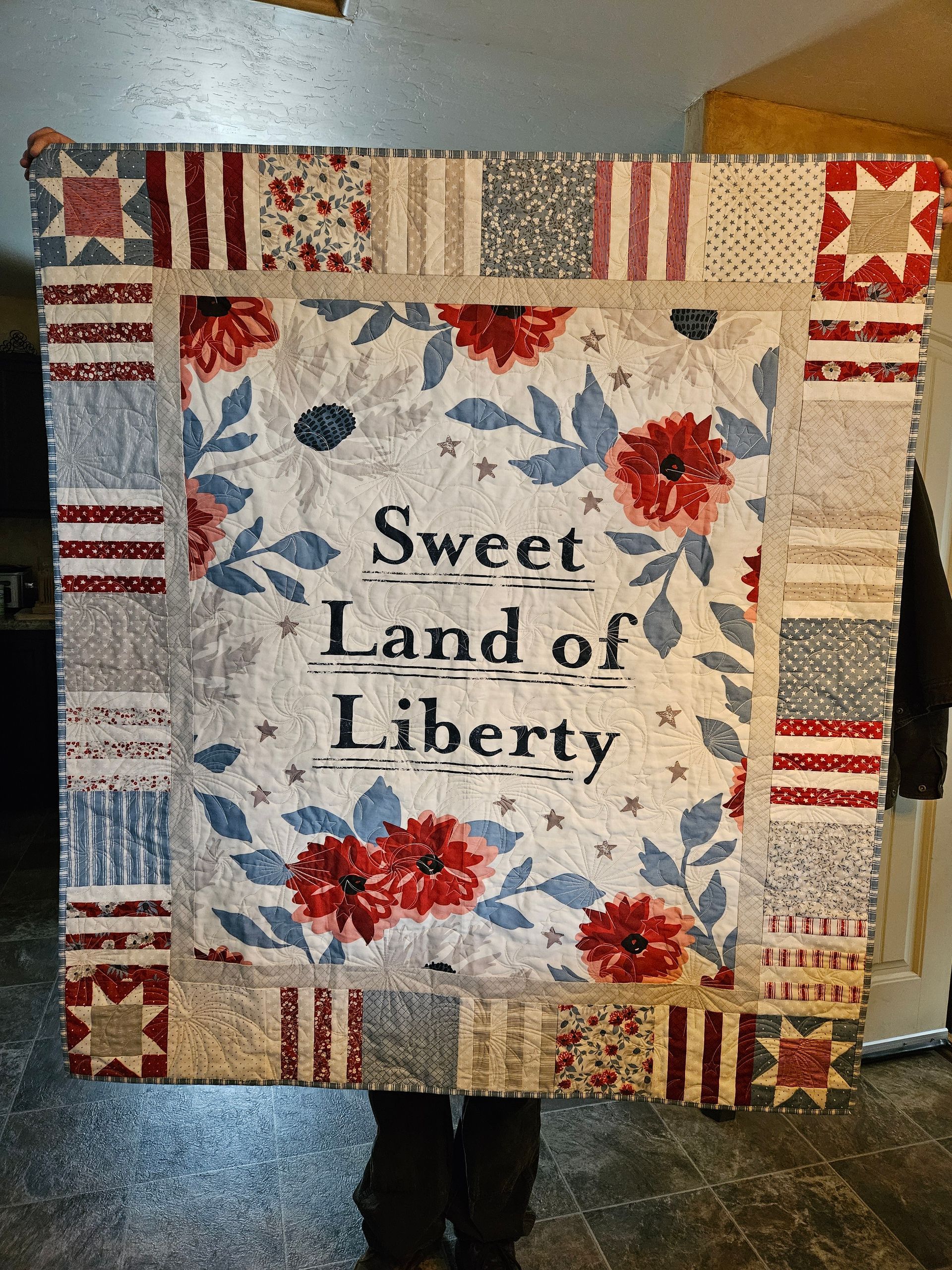 Quilted wall hanging with red, white, and blue blocks reading “Sweet Land of Liberty”