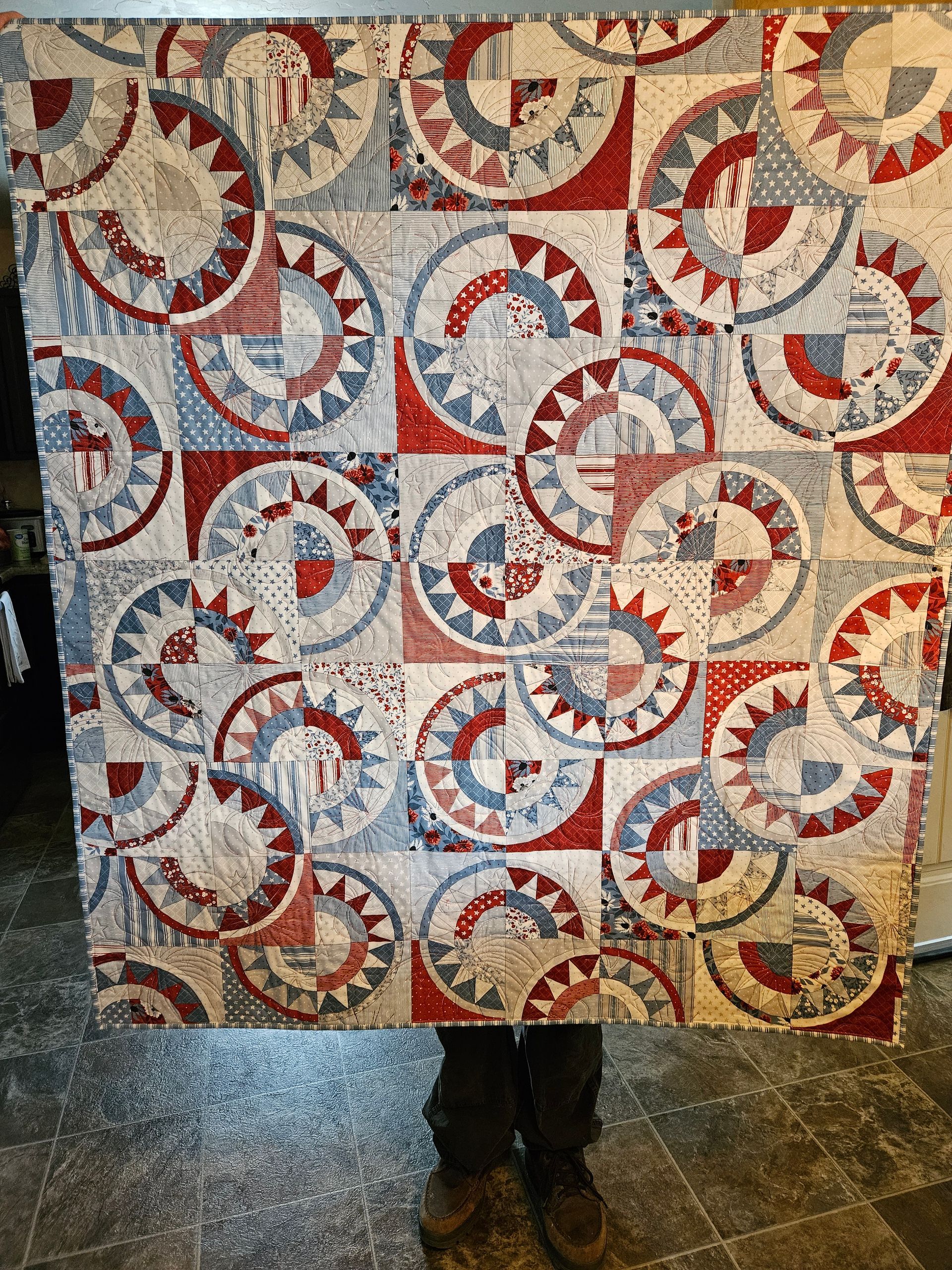 Person holding a colorful patchwork quilt with circular red, blue, and beige patterns indoors