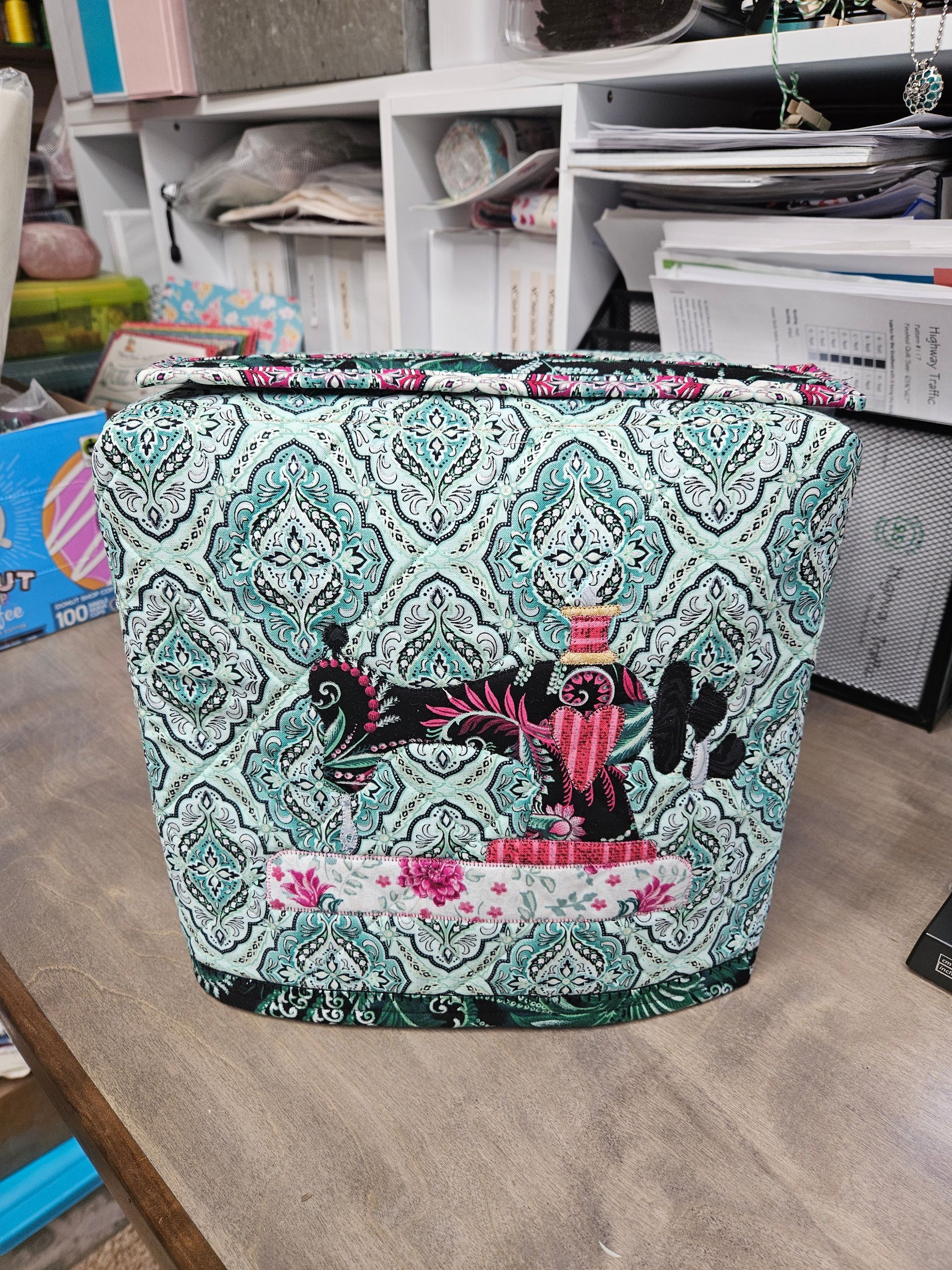 Teal patterned tote bag with pink and black lettering on a table in a craft room