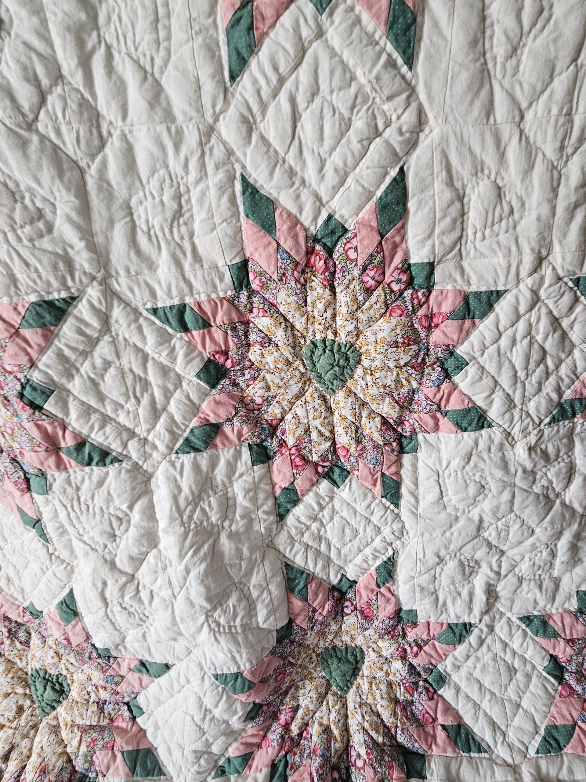 Close-up of a quilt with pink and green floral starburst patterns on a white stitched background