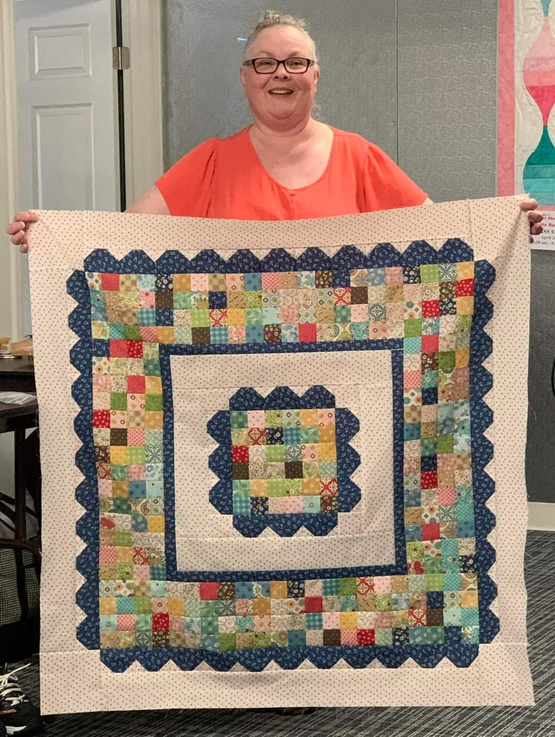 Person holding a colorful patchwork quilt indoors, smiling at the camera.