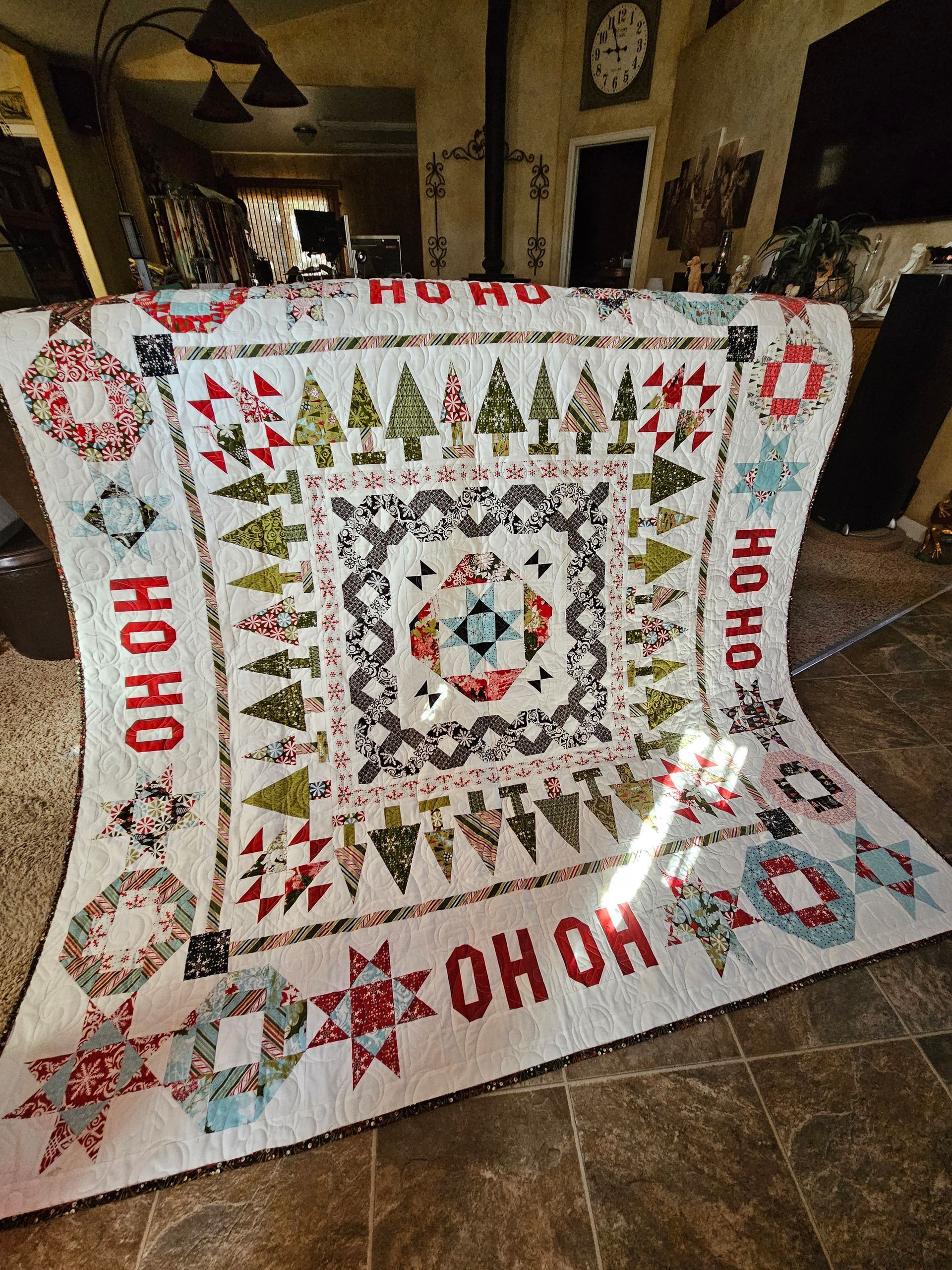 Christmas quilt with “HO HO HO” text, featuring trees, wreaths, and a central holiday star pattern.