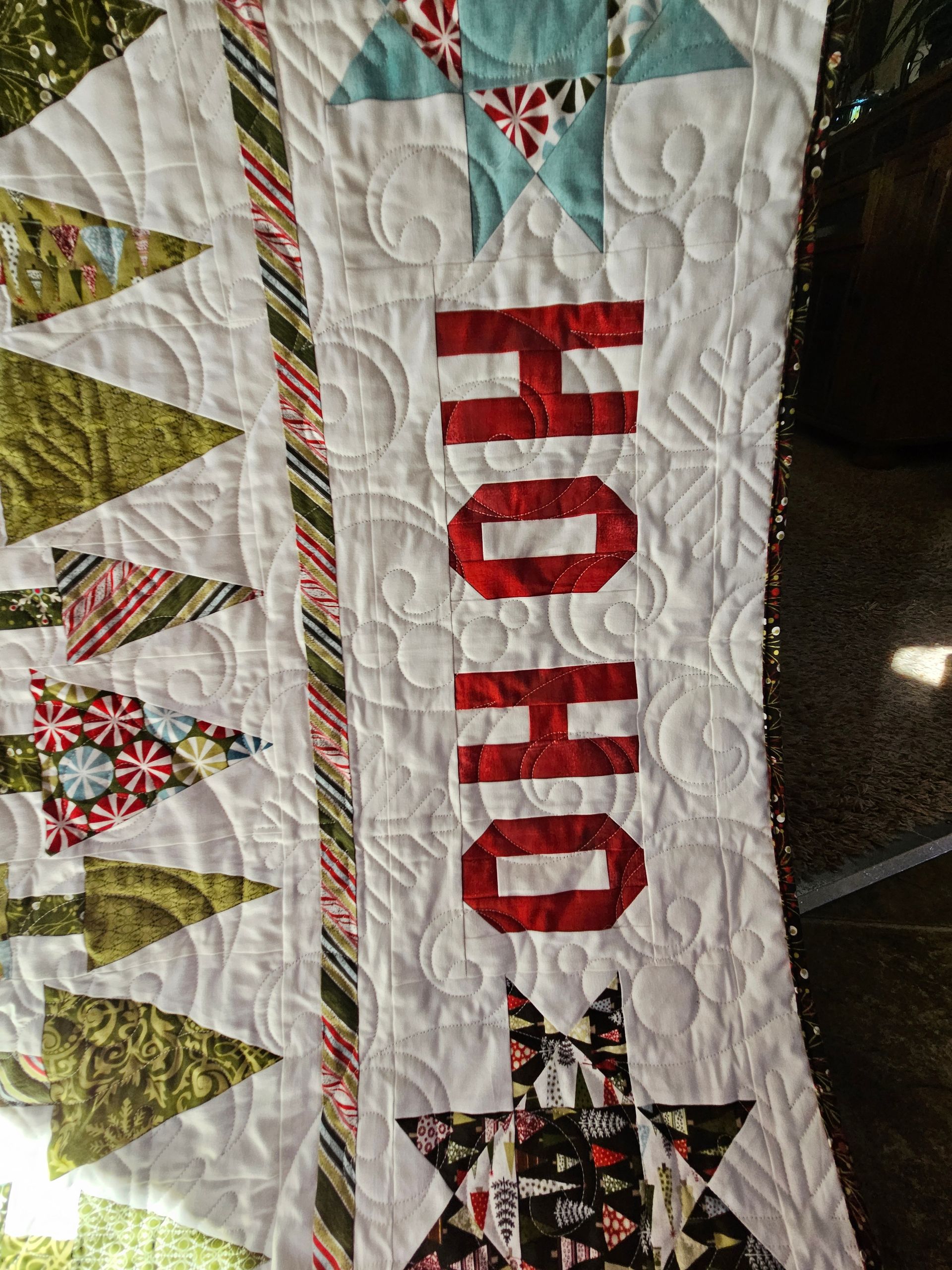 Quilted Christmas banner with red “HO HO” text and green trees on a white background
