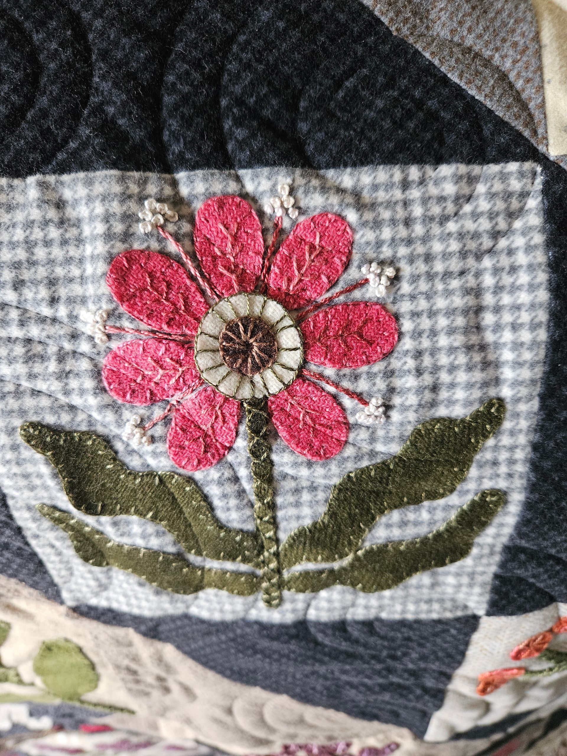 Pink flower embroidery on a gray quilt square with green leaves and dark patchwork borders