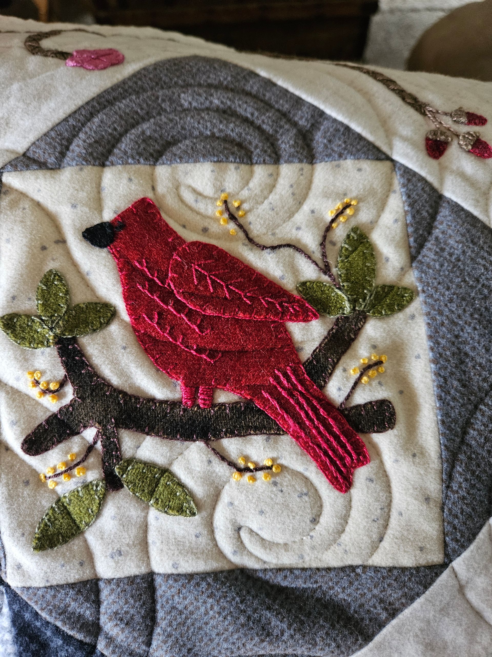 Red bird embroidery on a white and gray quilt with green leaves and gold accents