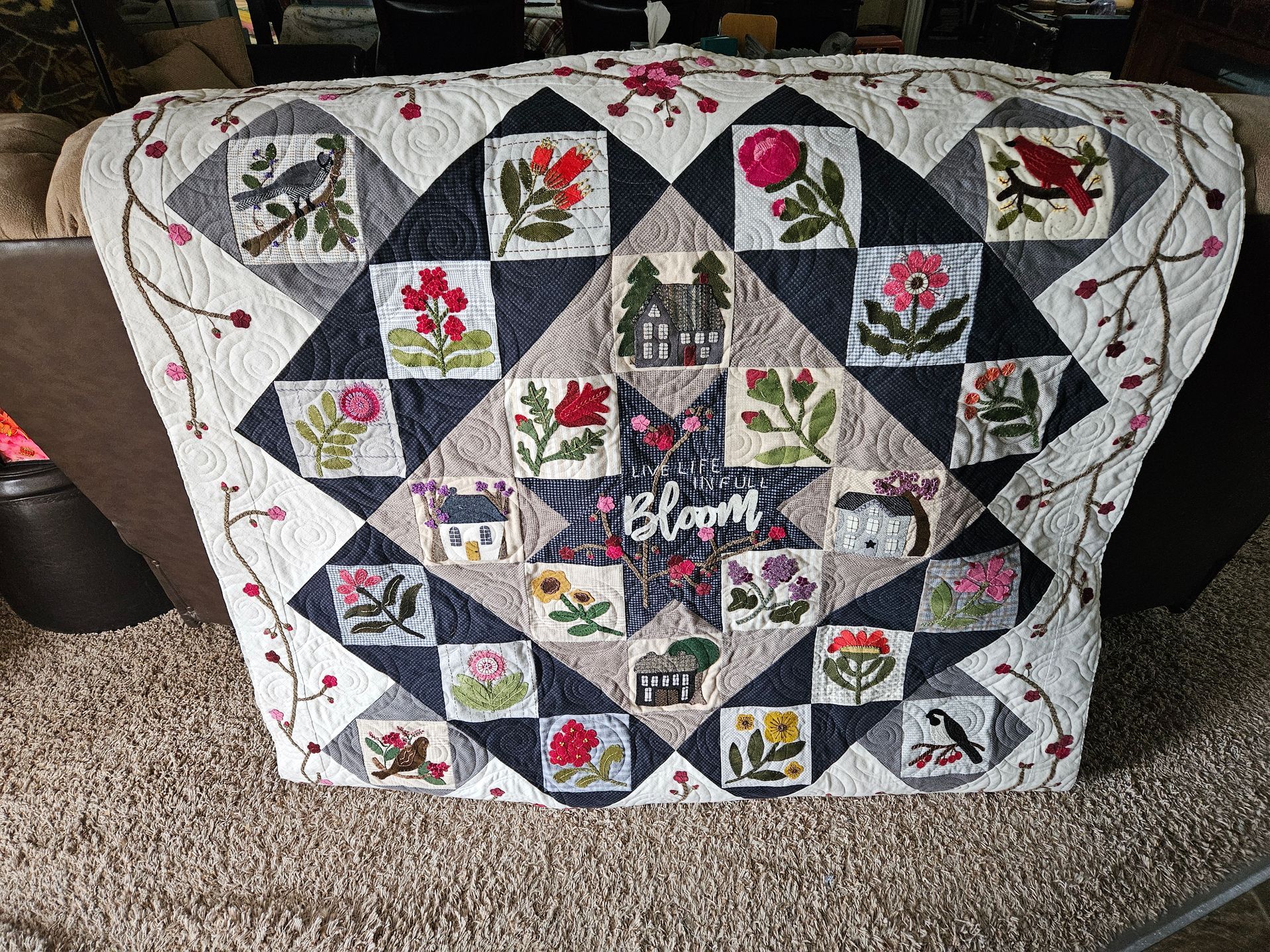 Colorful quilt draped over a chair, with patchwork squares, floral prints, and a central embroidered heart.