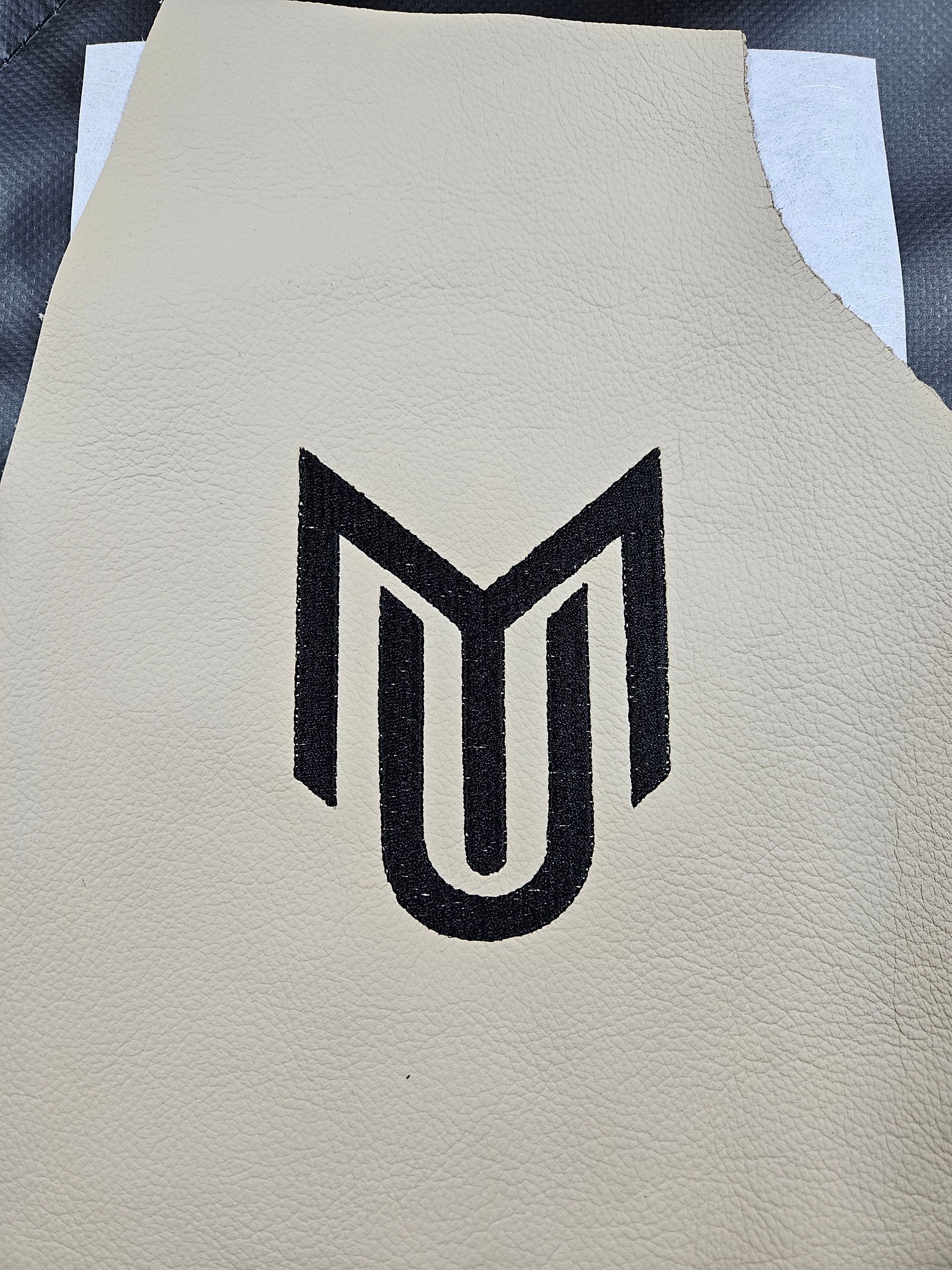 Black stylized MU logo on a light beige fabric surface.