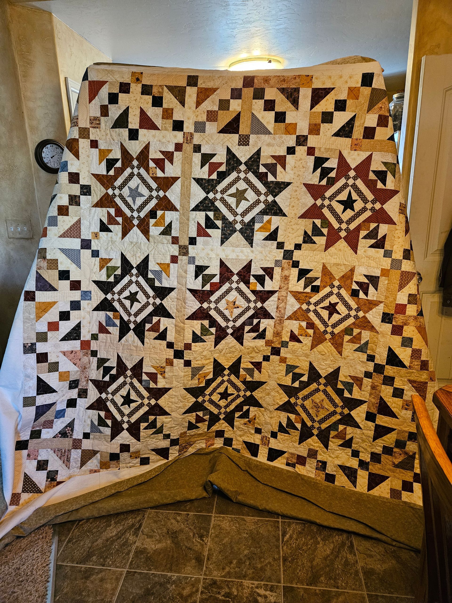 Patchwork quilt with starburst blocks in cream, brown, black, and gold, draped over a chair indoors