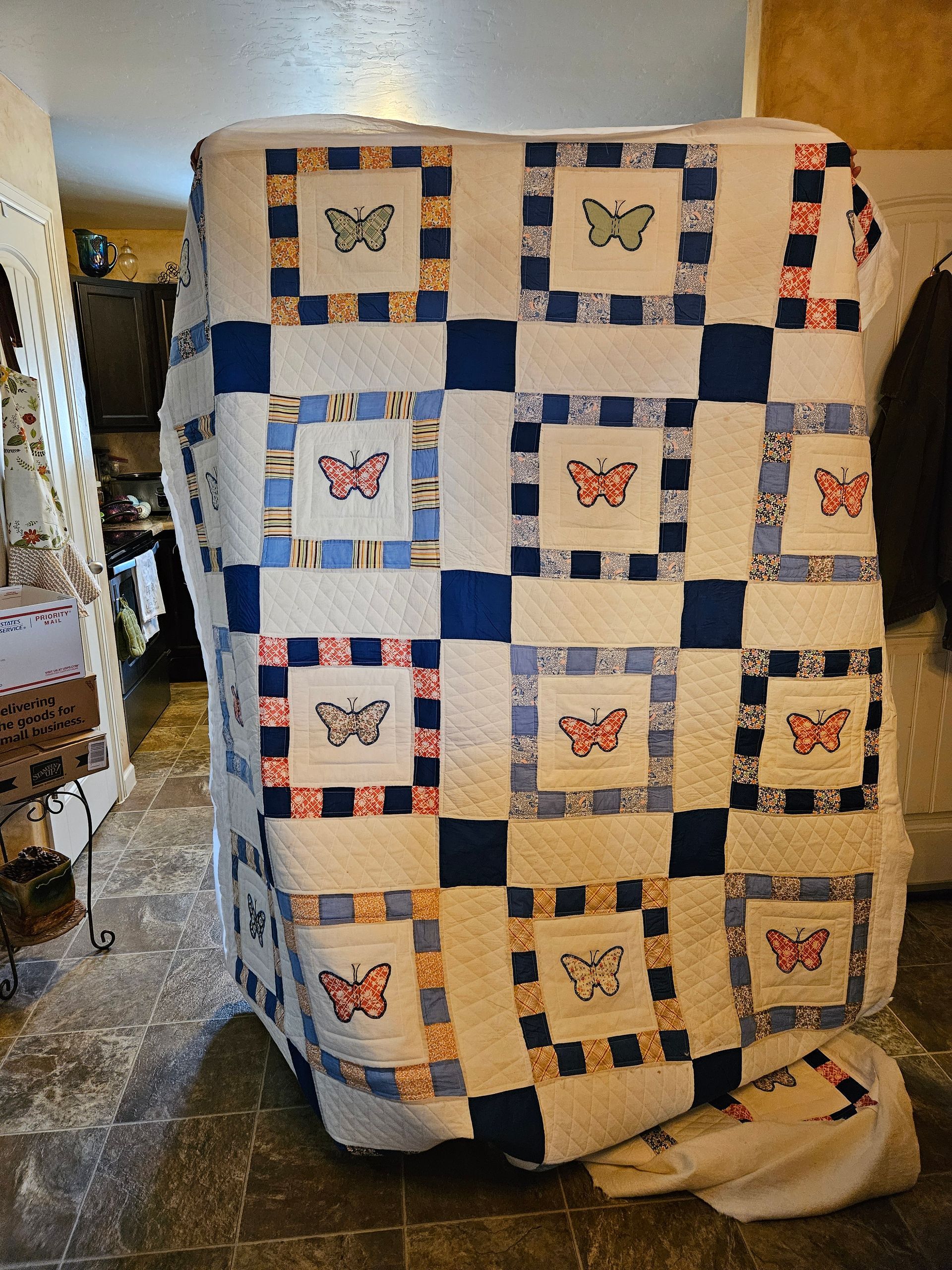 Quilted blue-and-white patchwork blanket with butterfly squares draped over a chair in a room