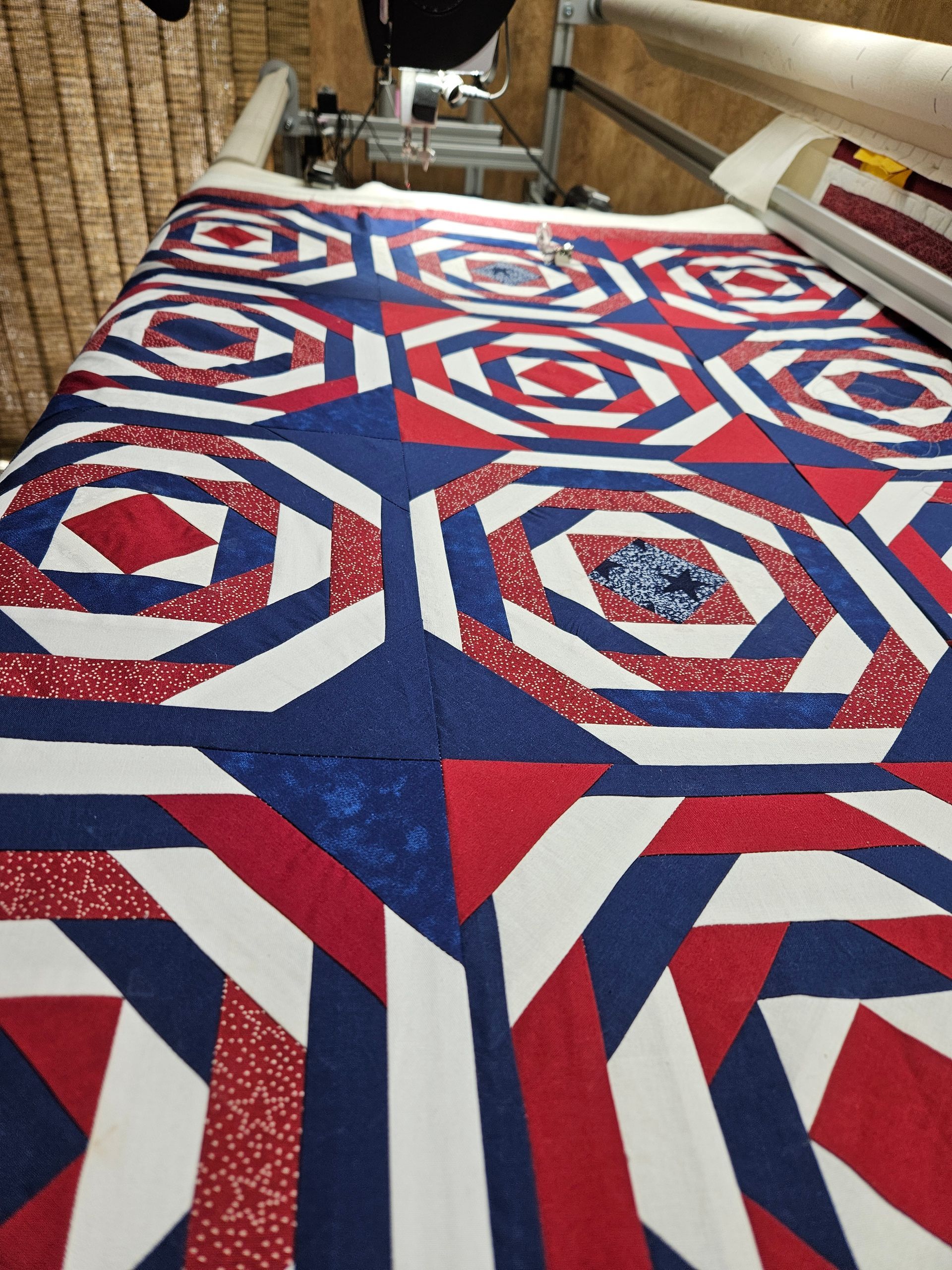Red, white, and blue geometric quilt laid out on a wooden floor and table frame.