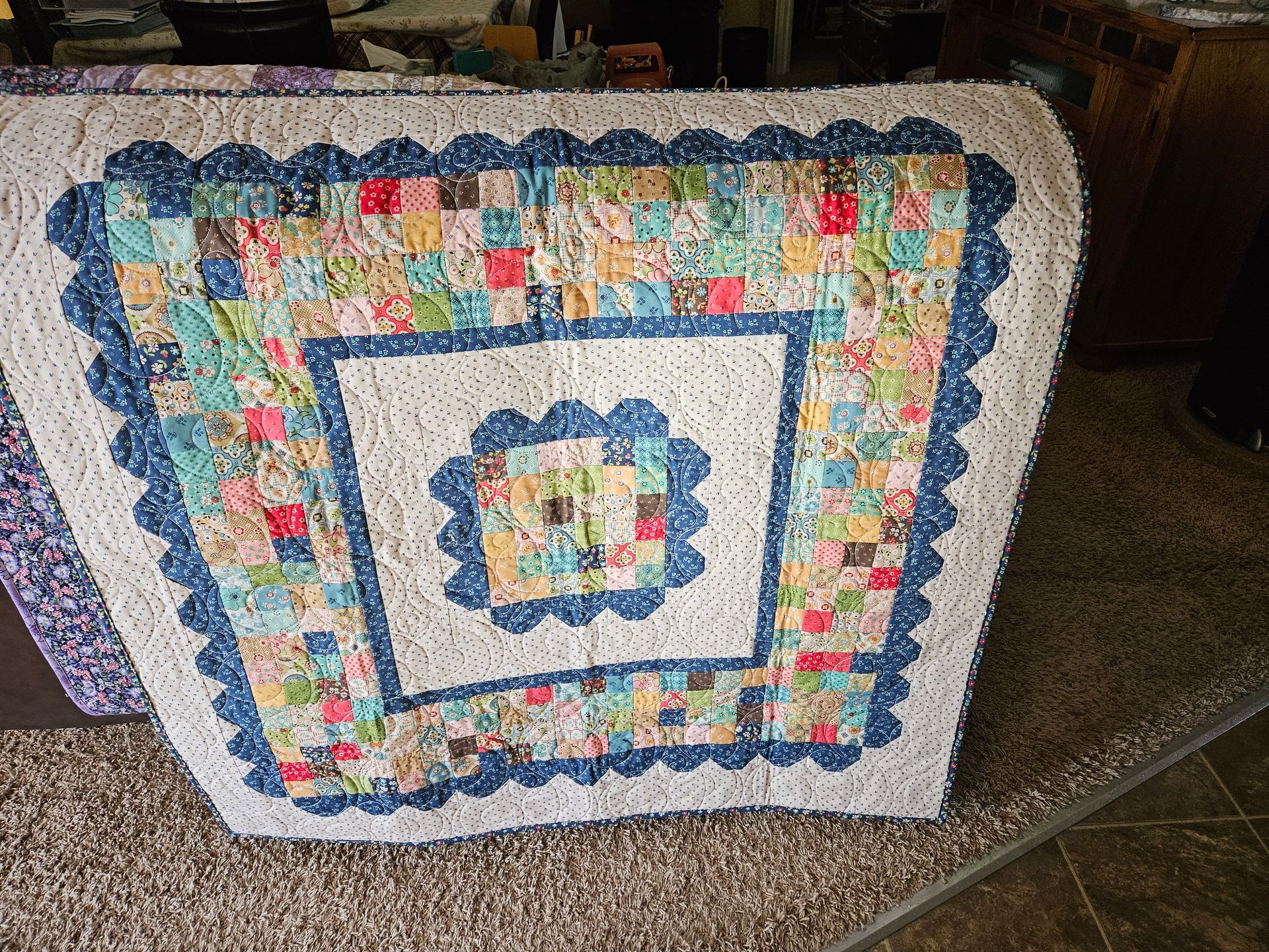 Colorful handmade quilt with a blue border and patchwork center draped over a chair