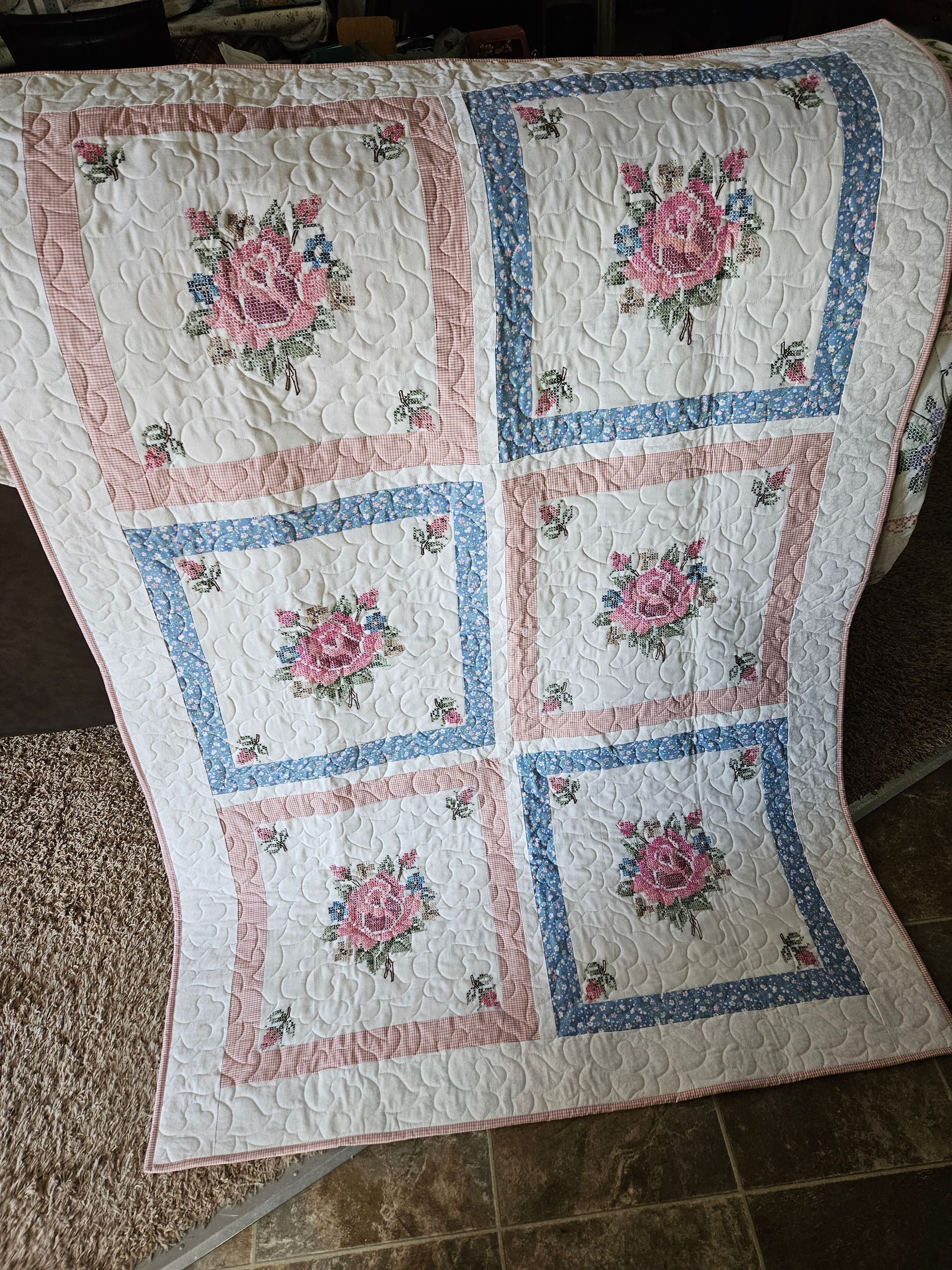 White quilt with pink floral squares and blue borders draped over a chair
