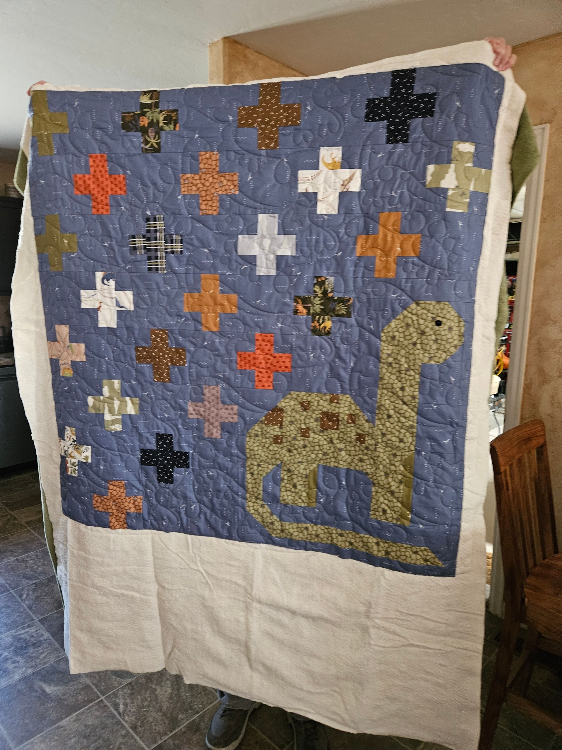 Patchwork quilt with multicolored plus signs and a gold giraffe on a blue background, draped over a chair.