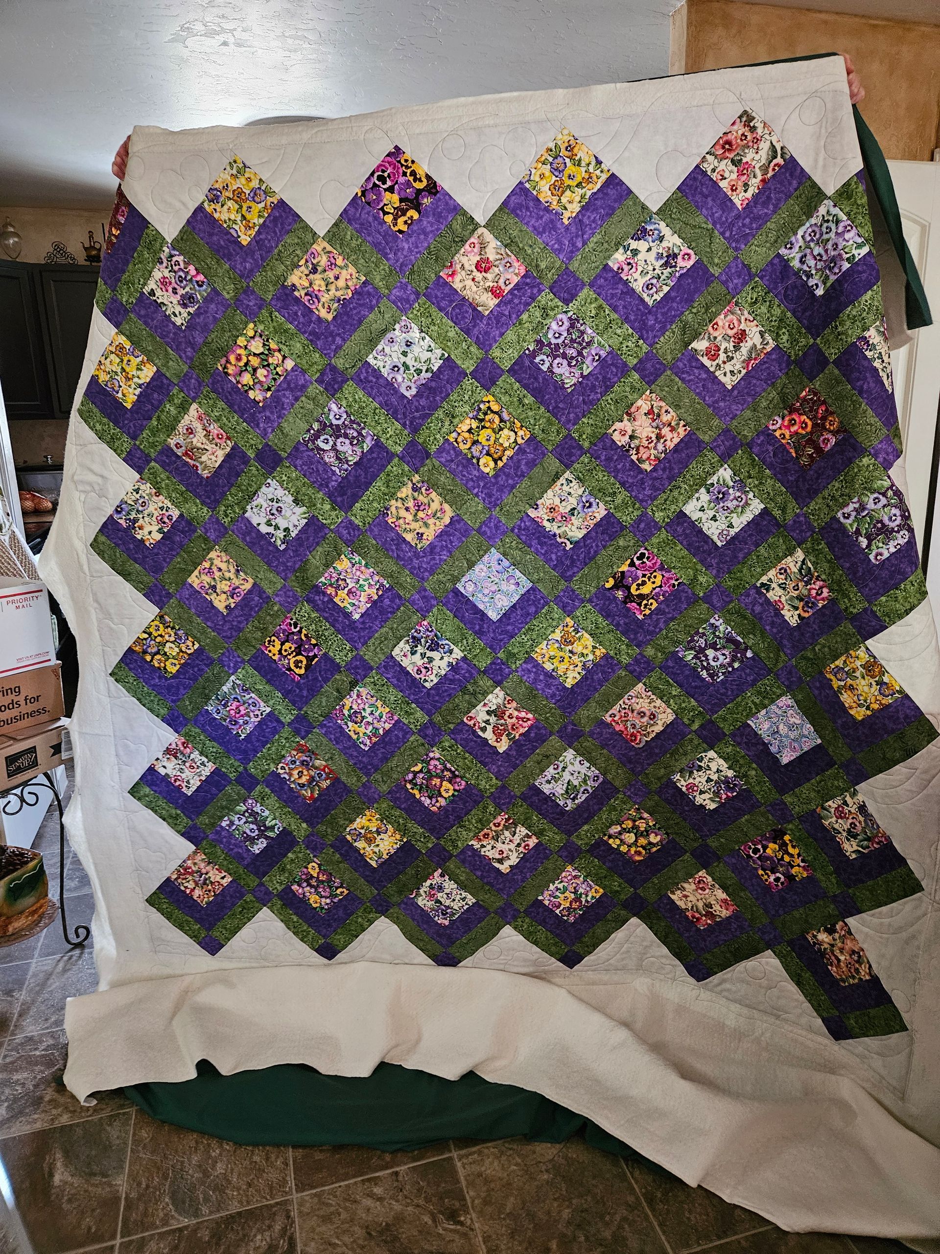 Colorful quilt of purple, green, and white diamond patches draped over a chair.