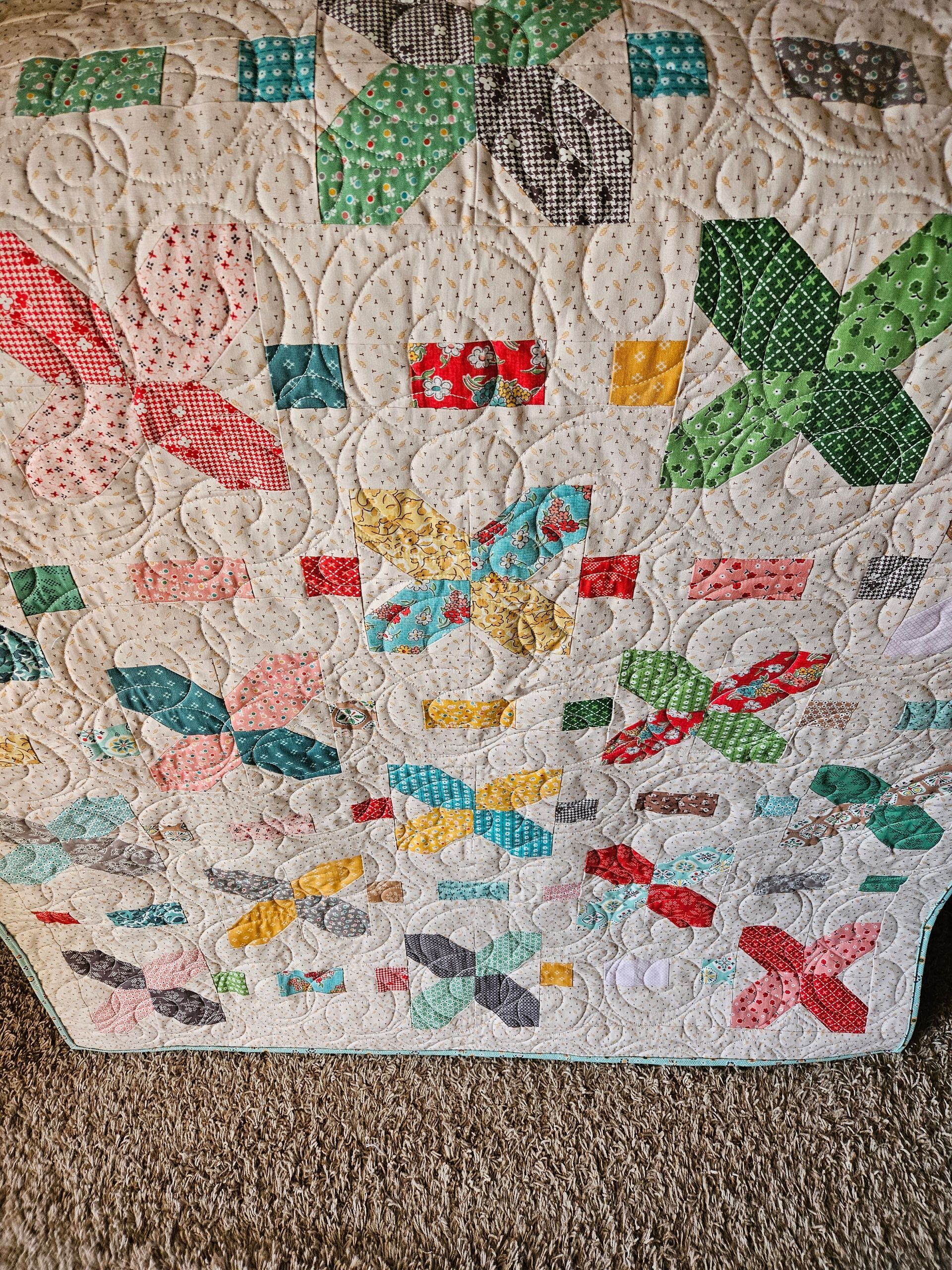 Colorful patchwork quilt with floral and leaf patterns on a carpeted floor