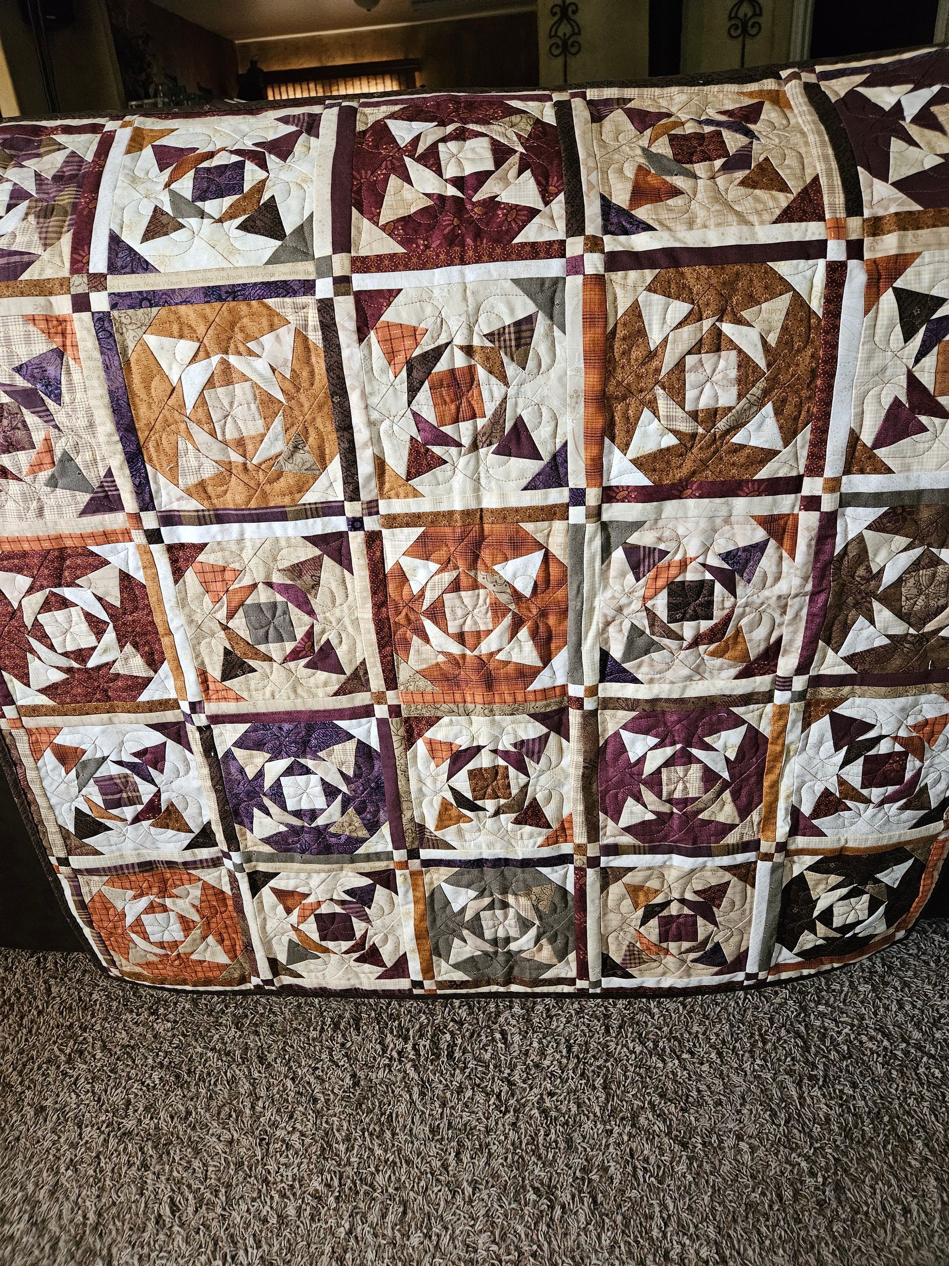 Patchwork quilt with autumn-colored star and square patterns draped over a chair.