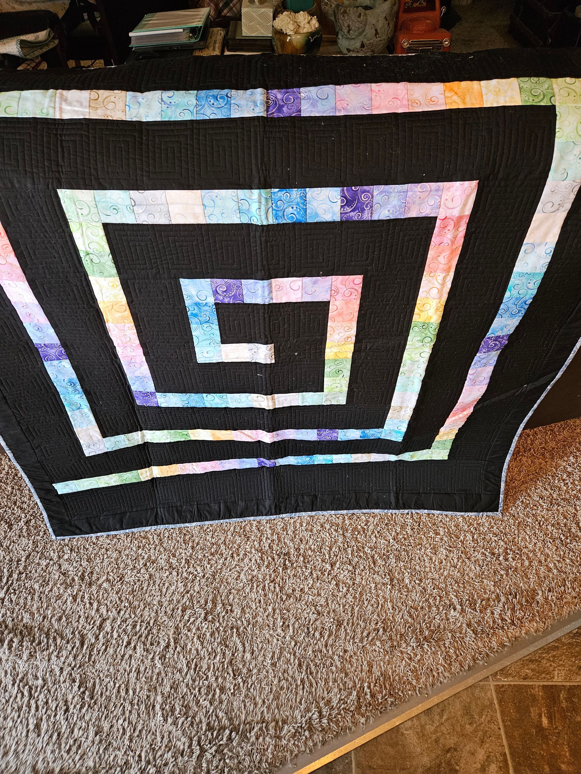 Black-and-white geometric spiral quilt draped over a chair on a carpeted floor.