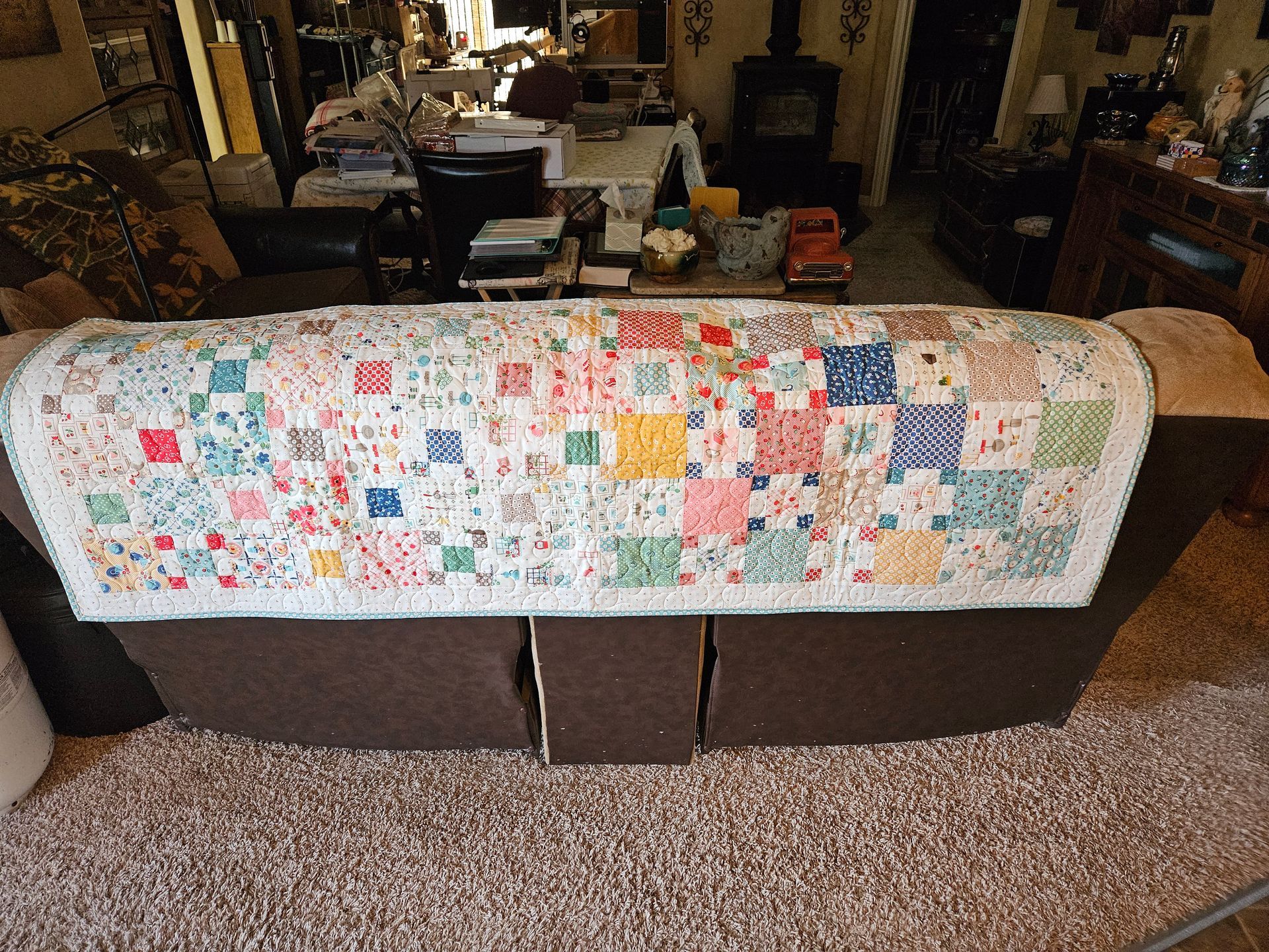 Colorful patchwork quilt draped over a brown couch in a cozy living room.