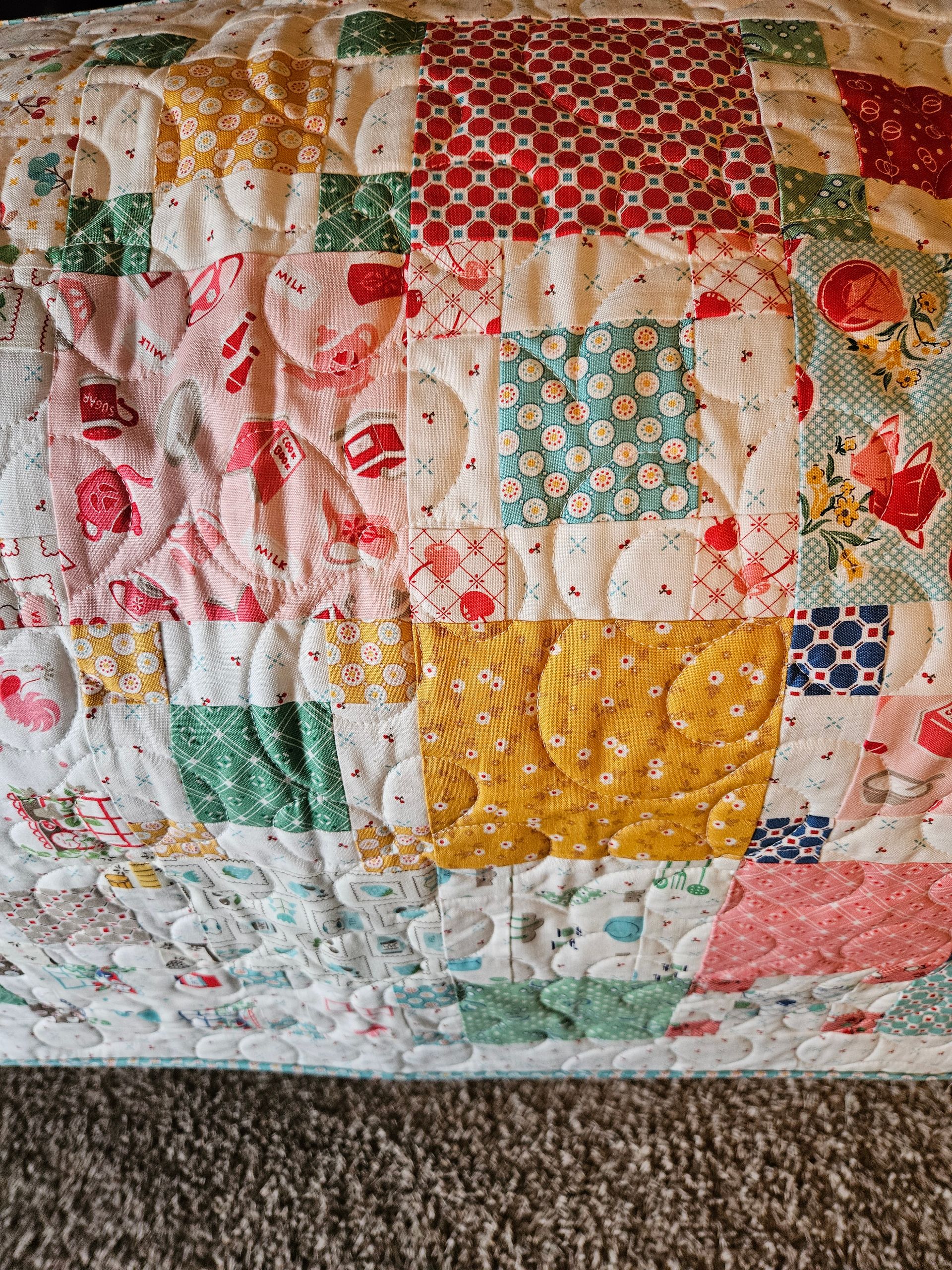 Colorful patchwork quilt with floral and patterned fabric squares on a carpeted surface