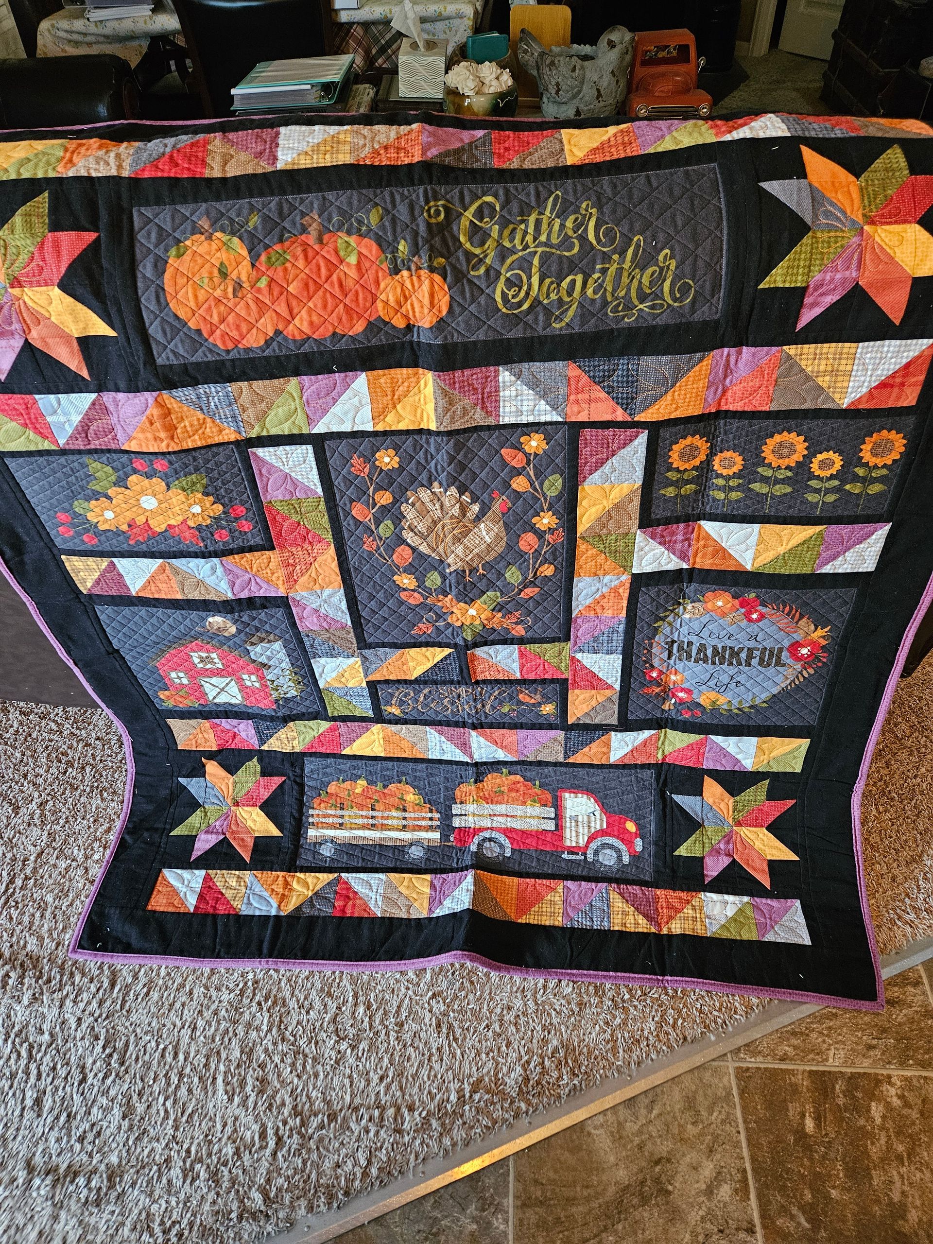 Colorful quilt with pumpkin and autumn leaf patches displayed on a carpeted floor