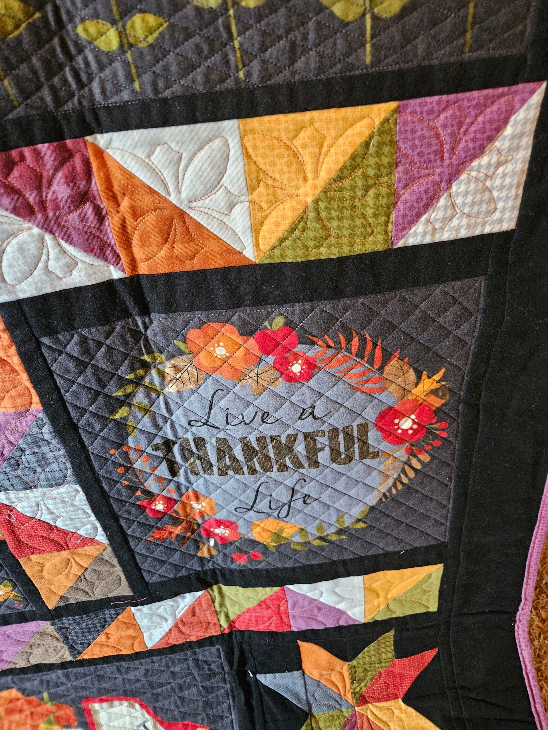 Colorful quilt with black borders and triangular patches, featuring a floral oval centerpiece.