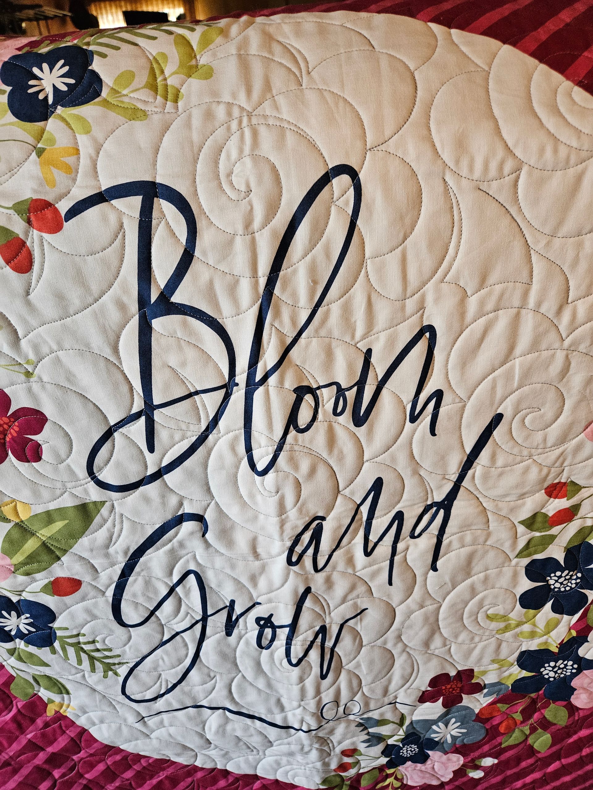 Quilted floral wall hanging with the words “Bloom and Grow” in navy script.