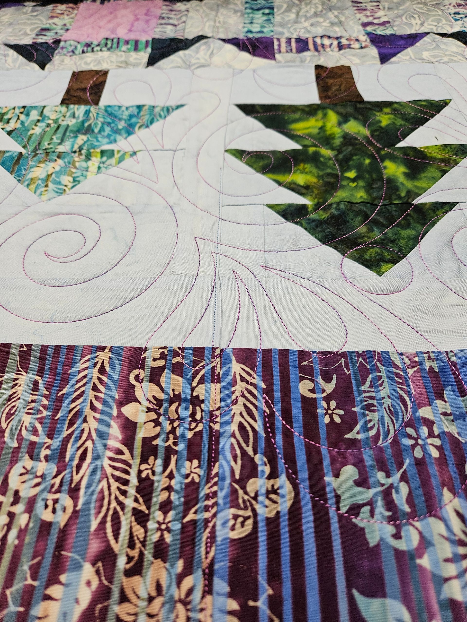 Patchwork quilt with white spiral quilting, green patterned triangles, and purple striped fabric.