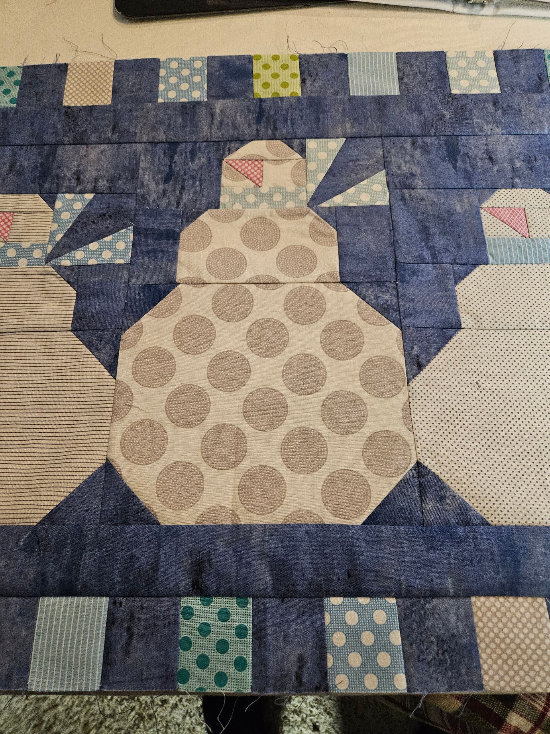 Patchwork quilt with a central snowman in blue and cream, bordered by striped fabric squares.