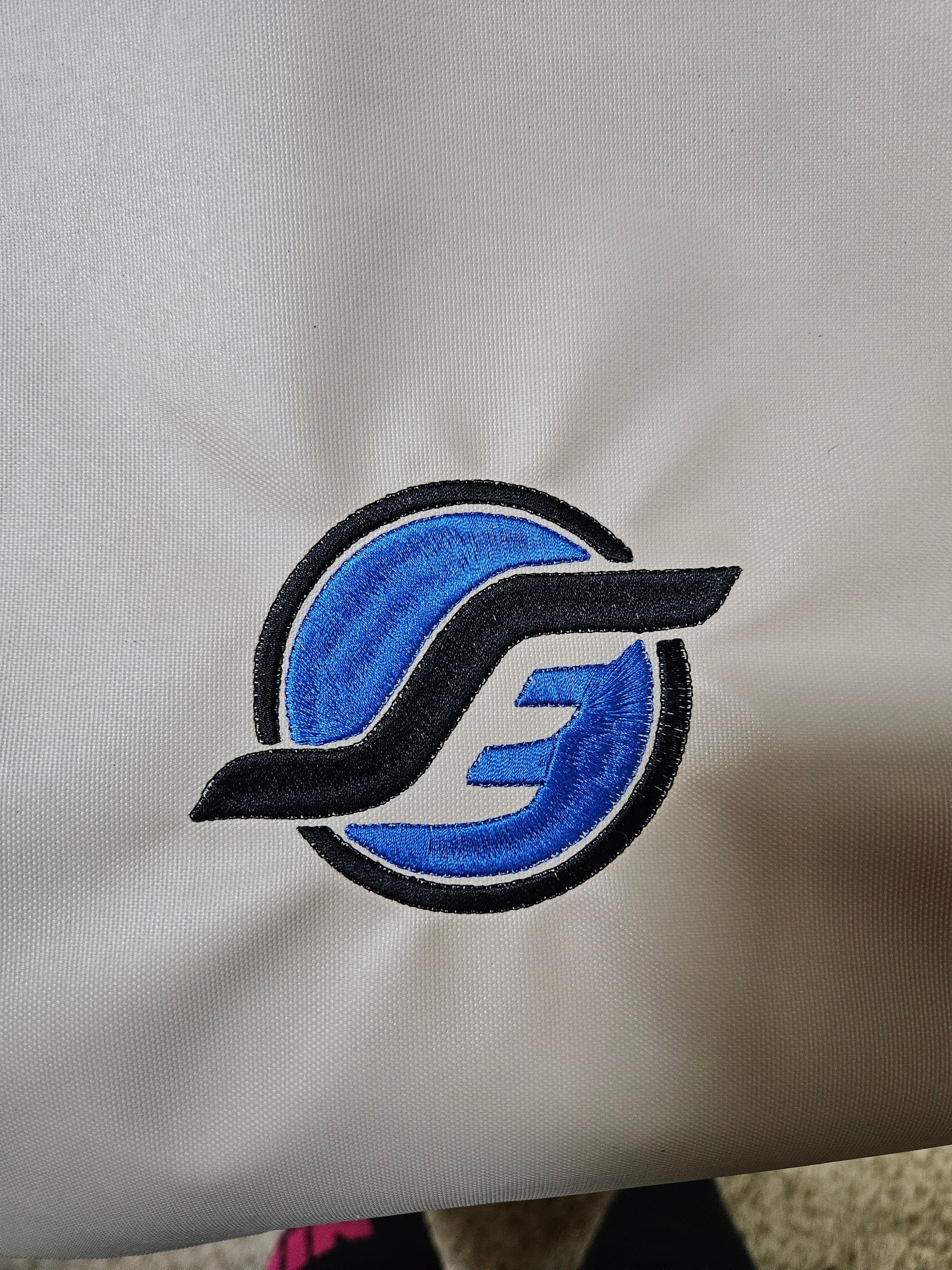 Blue and black circular logo embroidered on white fabric