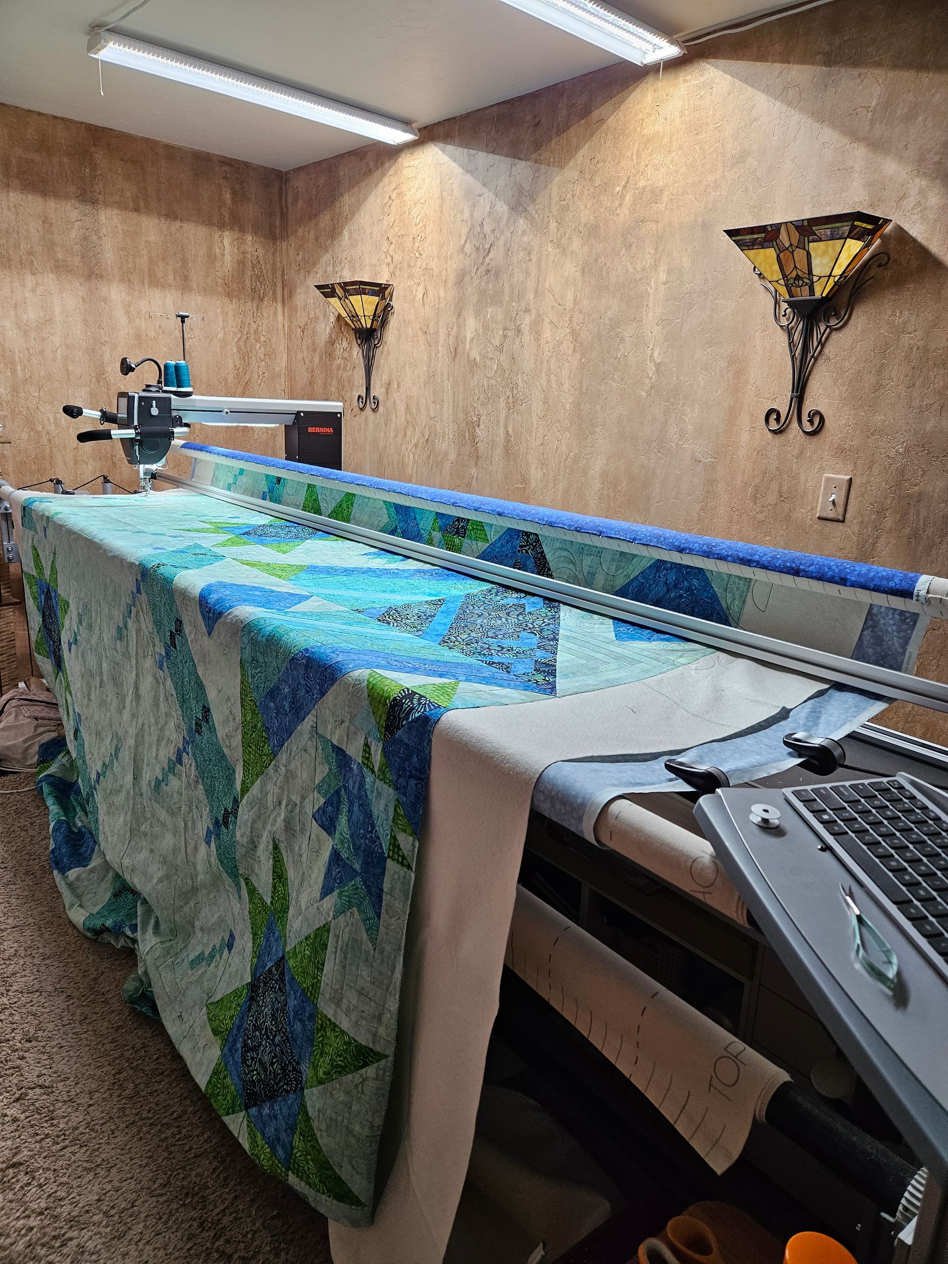 Long-arm quilting machine stitching a colorful quilt in a small wood-paneled room