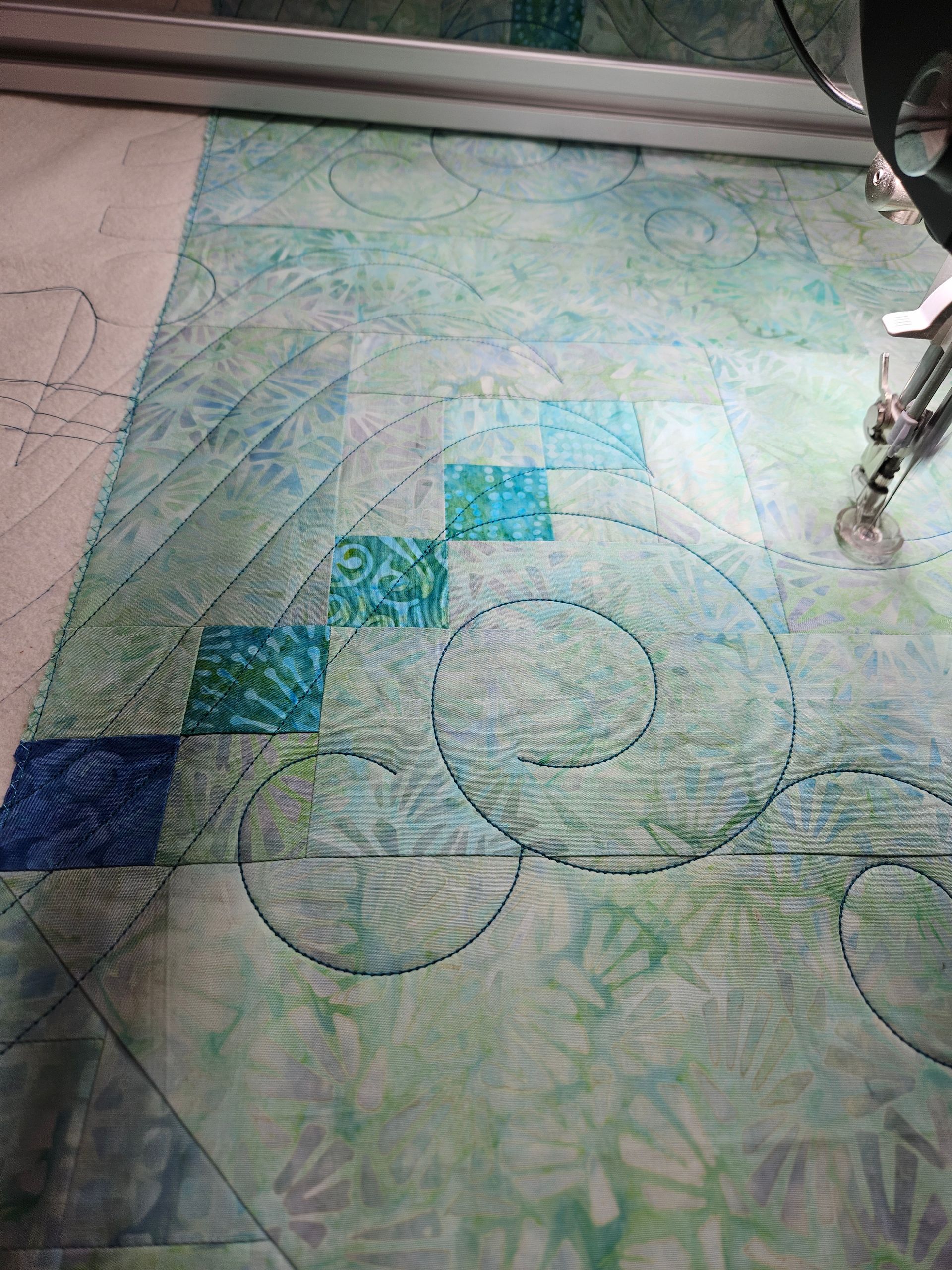 Quilted patchwork fabric with blue-green squares and circular stitched patterns on a table.