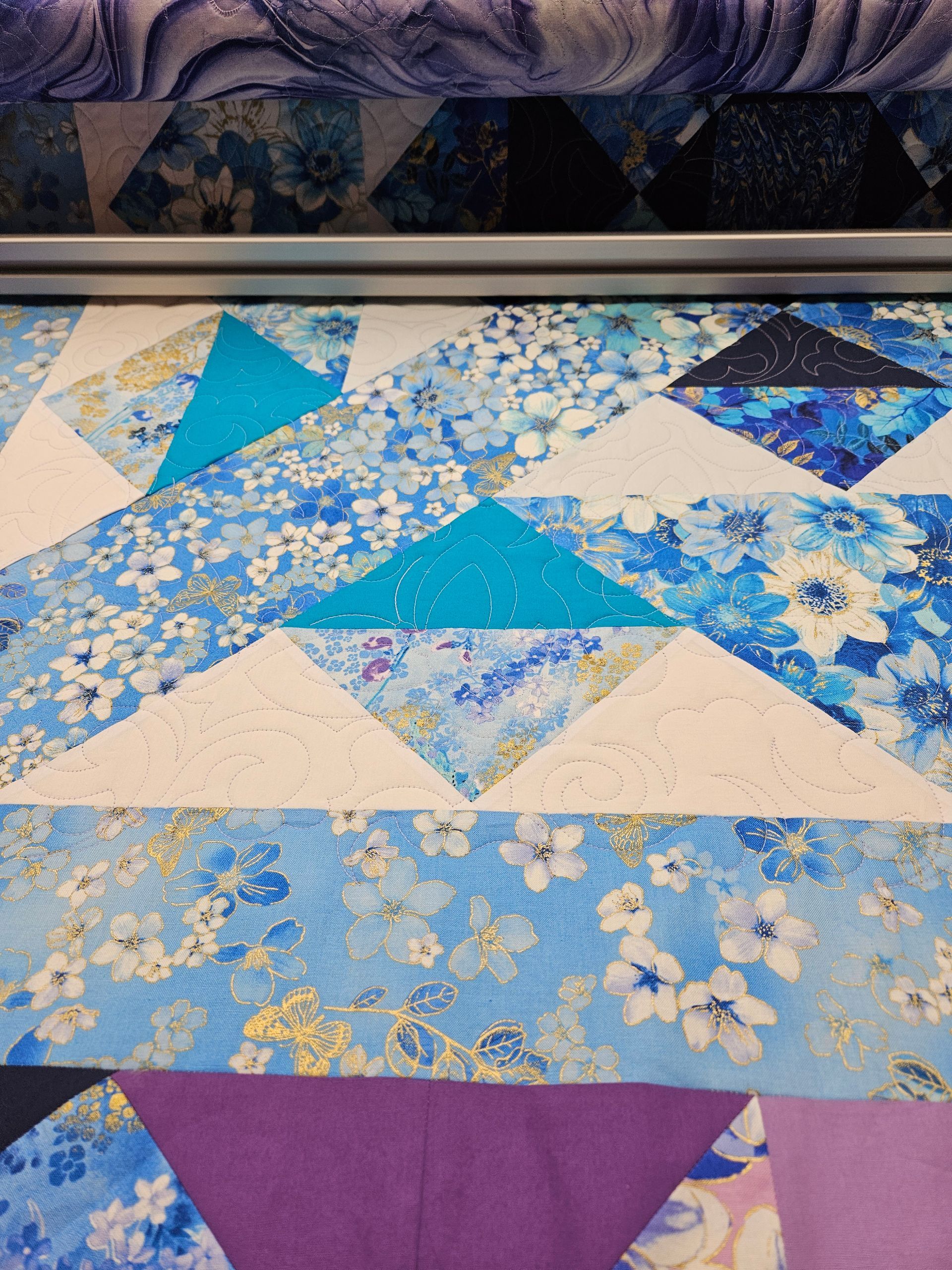 Blue and white geometric quilt with floral patterns and purple accents