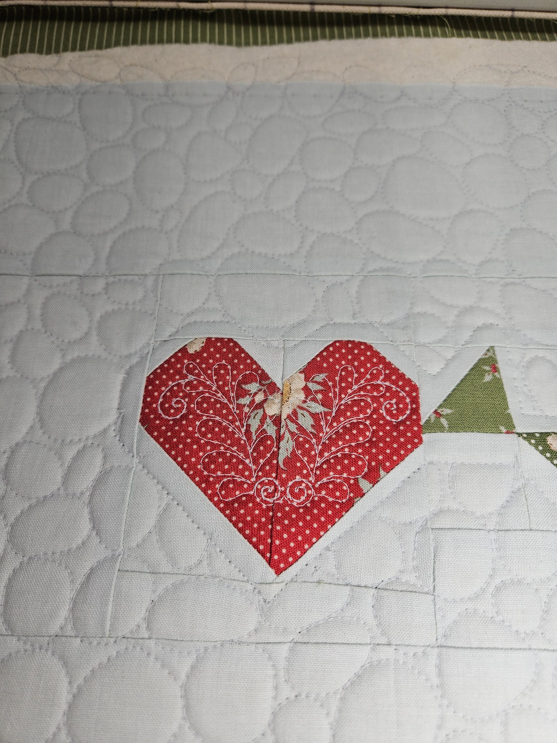 Red heart patchwork on white quilt with a small green triangle to the right.