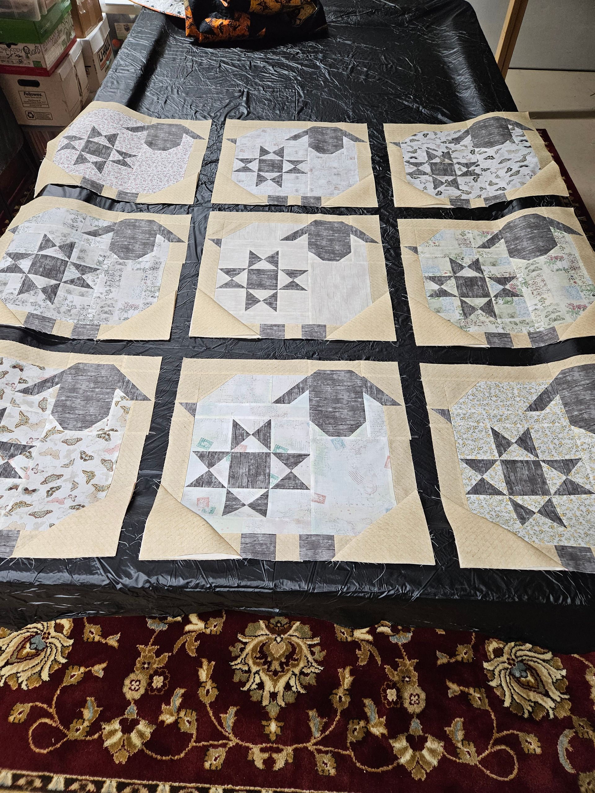 Patchwork quilt with beige, gray, and black geometric blocks laid on a patterned carpet.